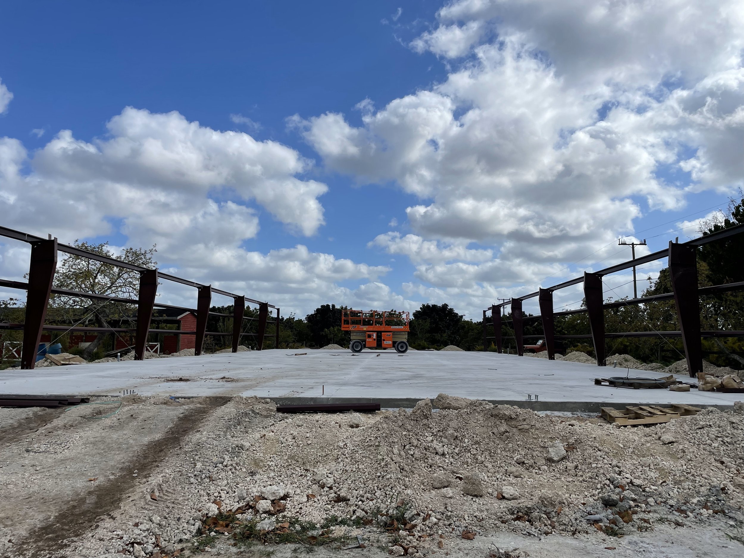 Construction site with a concrete slab, metal railing, and construction equipment under a cloudy sky.