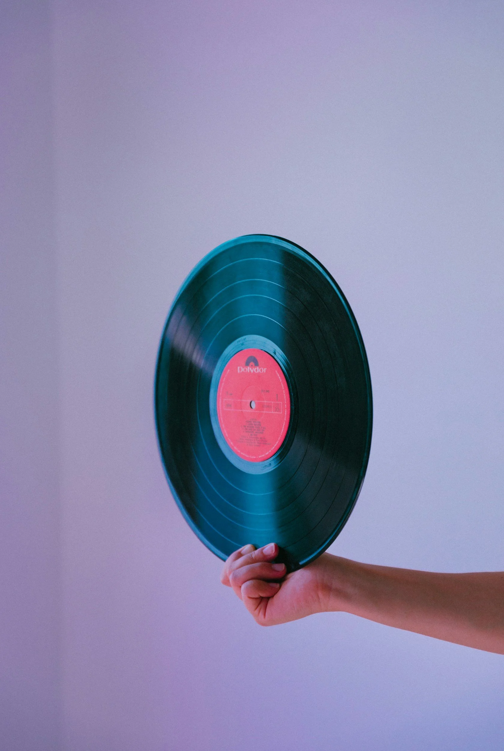 A hand holding a vinyl record against a plain background.
