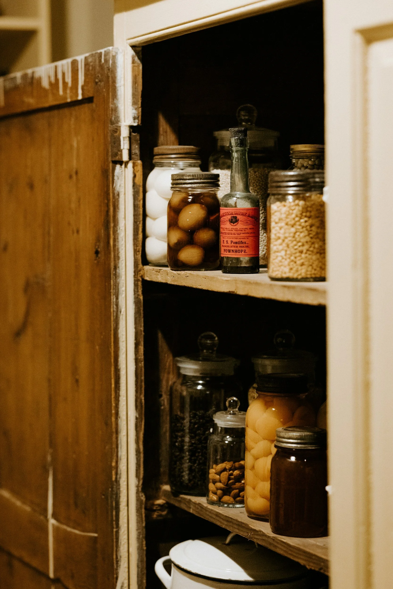 Kitchen cabinet with jars containing eggs, pickles, spices, and various food items.