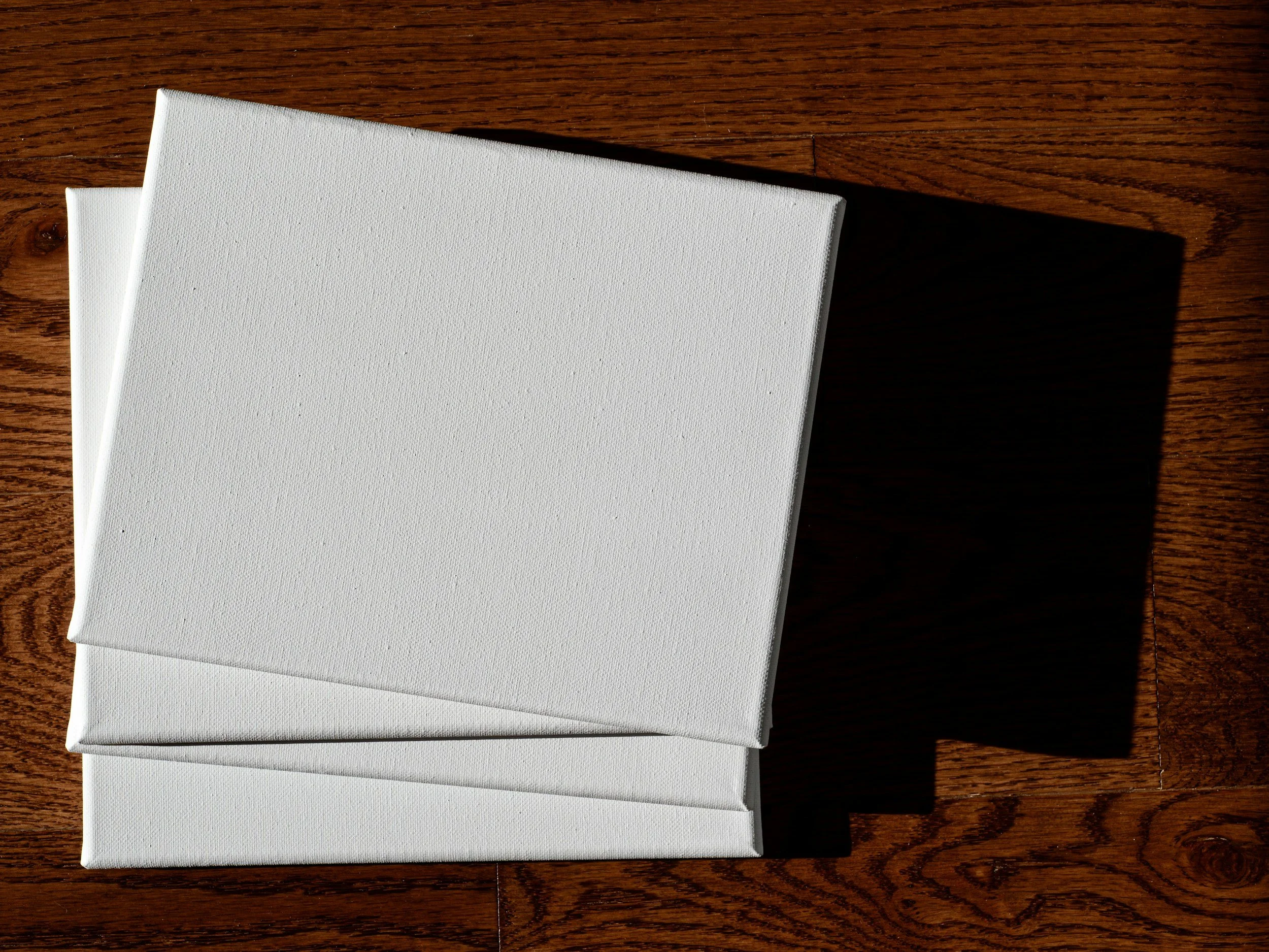 Two blank white canvases placed on a wooden surface.