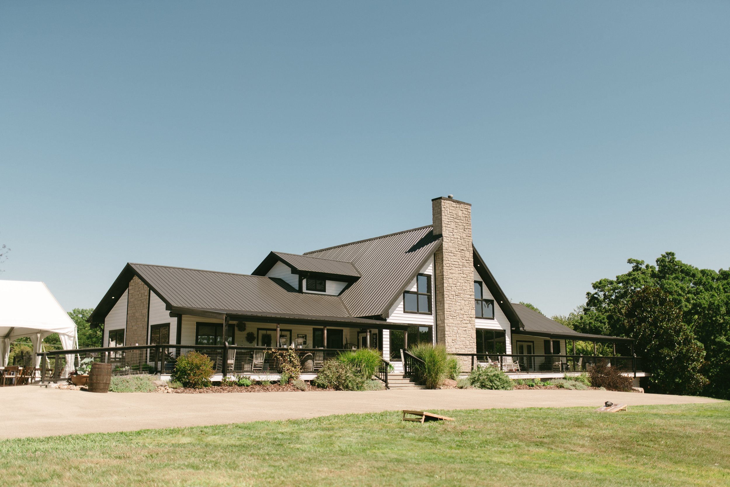Modern farmhouse with black metal roof, large windows, and wraparound porch.
