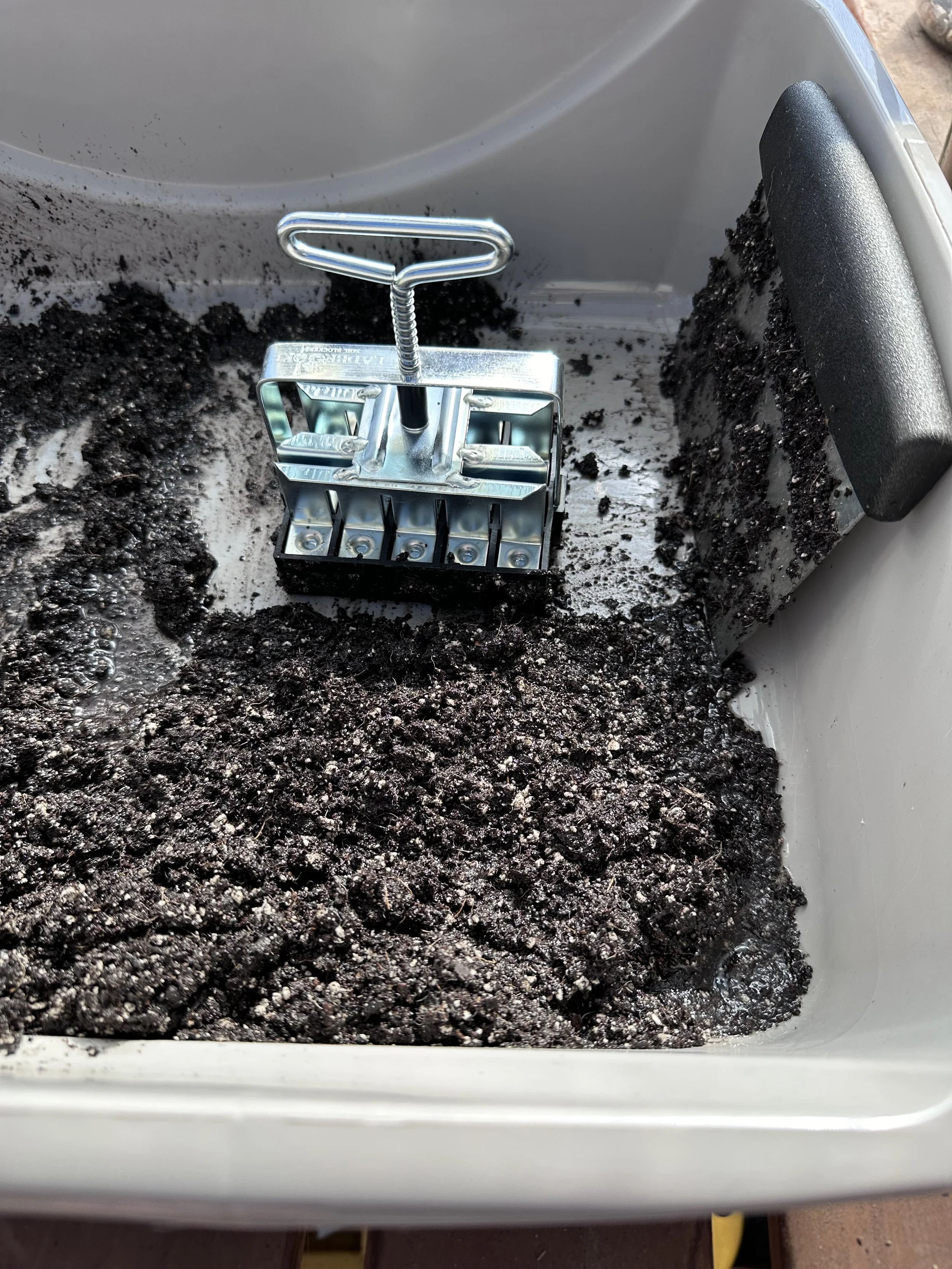 Soil blocker tool in a bin with soil