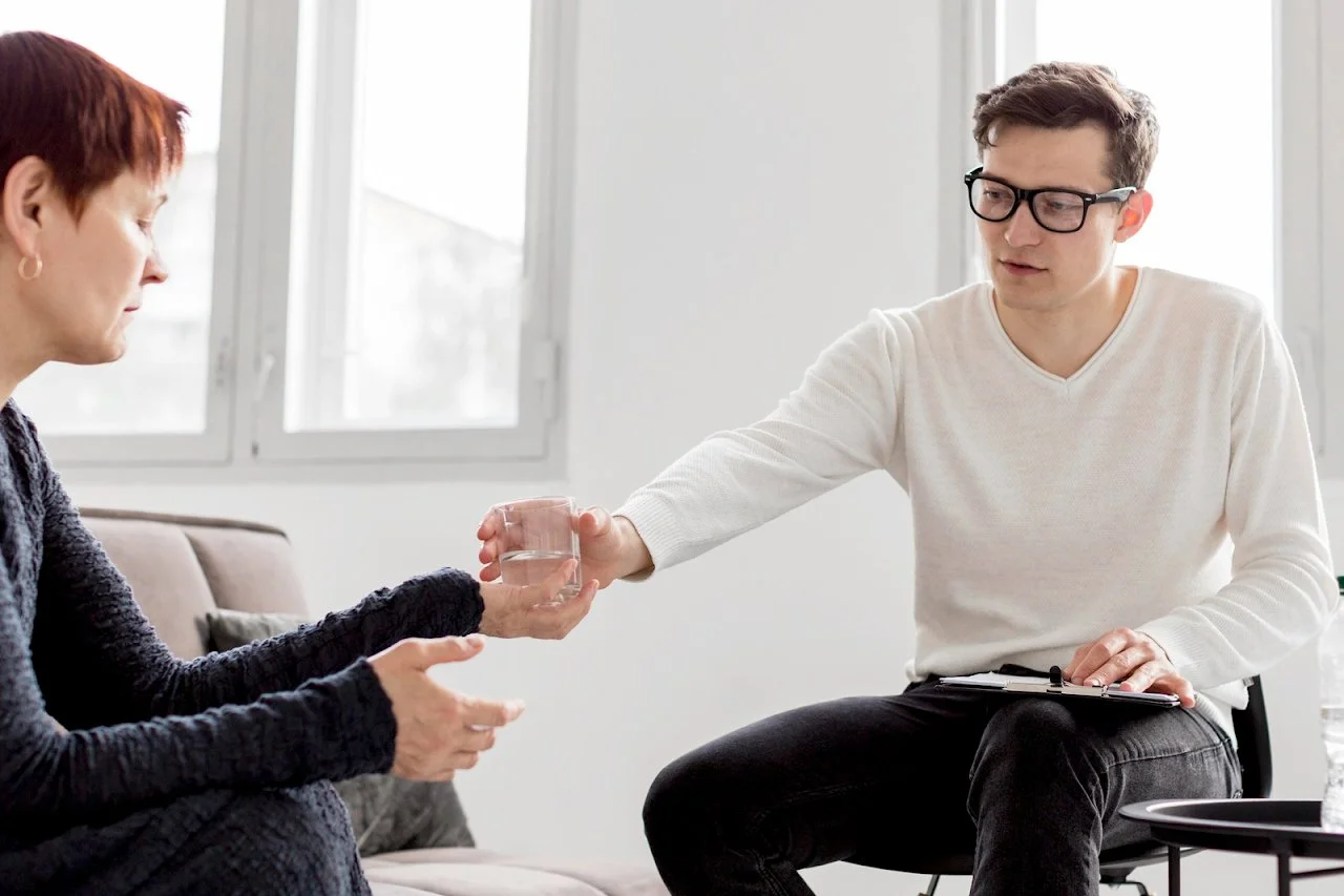 Male therapist offering a glass of water to a client during a counseling session, symbolizing empathy and professional mental health care.