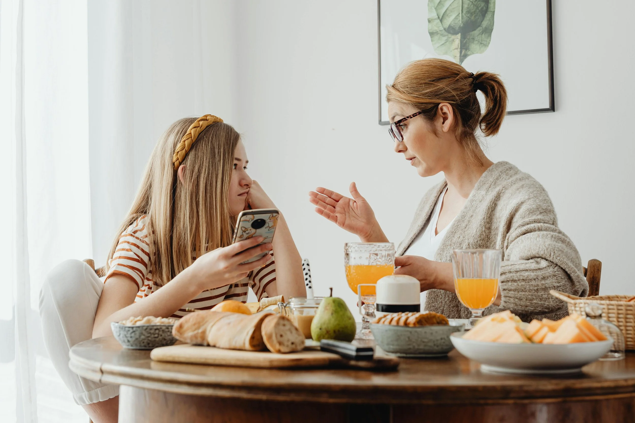 Mother discussing phone use with her teenage daughter at the breakfast table.