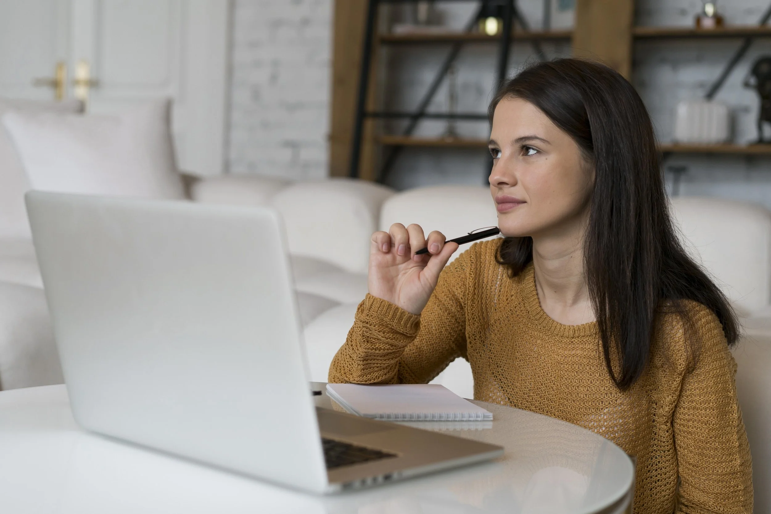 Woman in sweater thinking in front of laptop, making a short list of goals for a counseling consultation