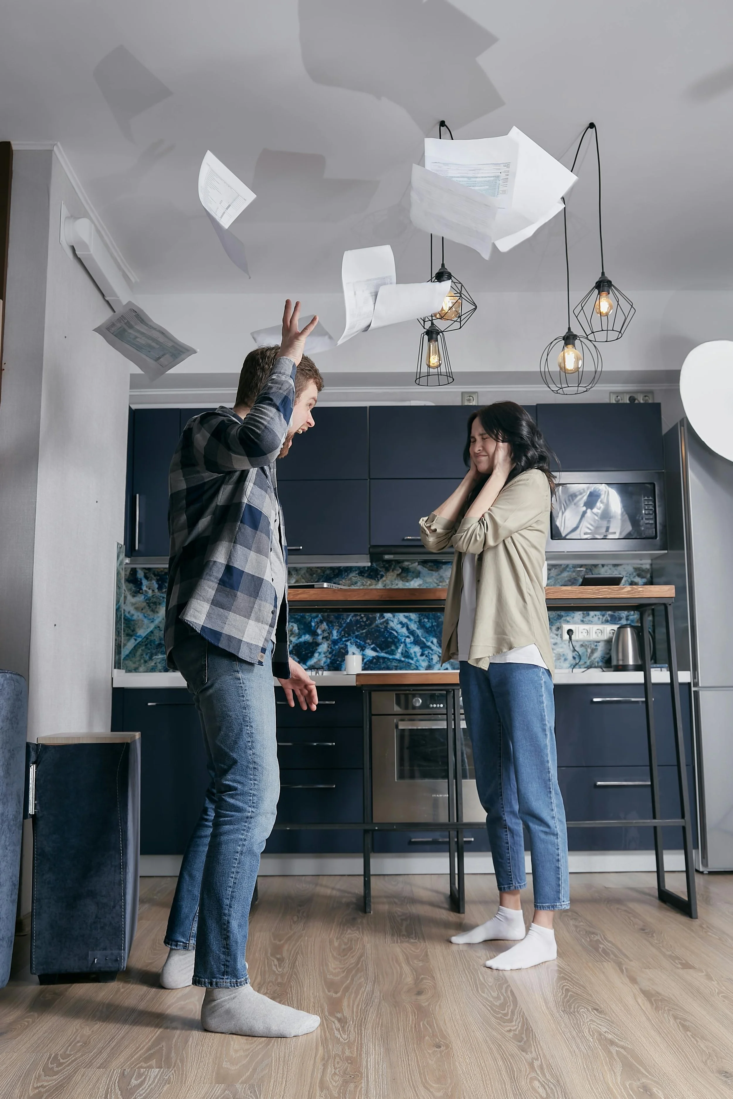Couple argues in a kitchen with papers flying, a scene suited to relationship counseling topics