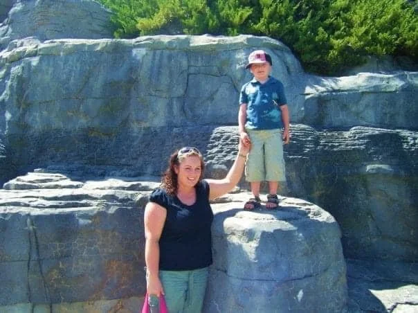 A woman holding the hand of a young boy standing on a large rock formation outdoors during daytime.