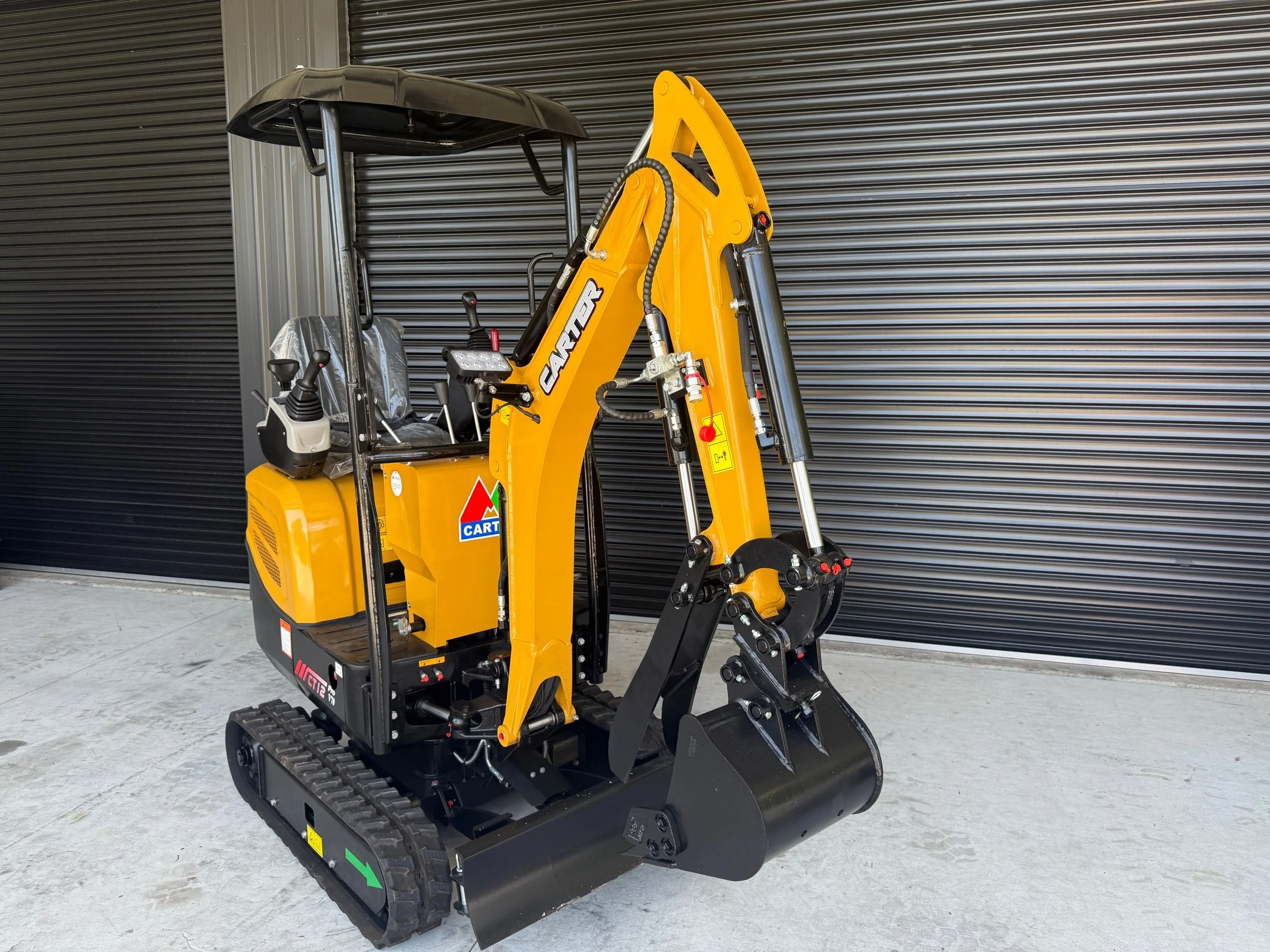 Yellow mini excavator with black tracks parked in front of a black corrugated metal wall.