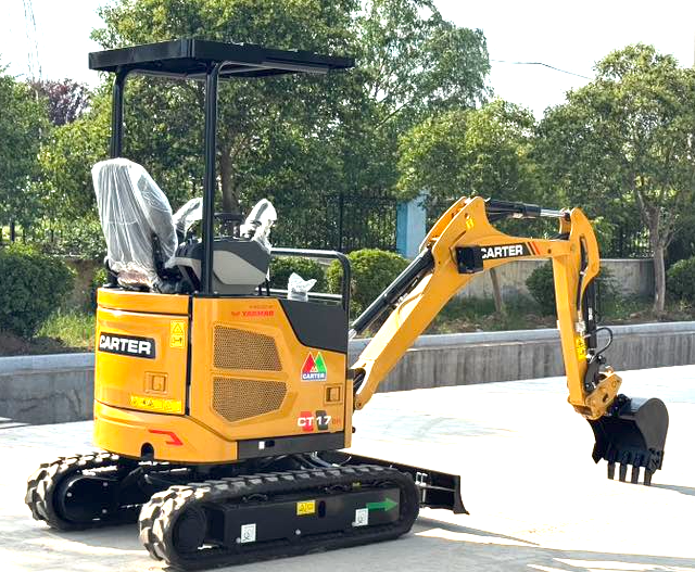 Small yellow excavator with a black tracked base, parked on a concrete surface, with in-progress construction or landscaping site background.