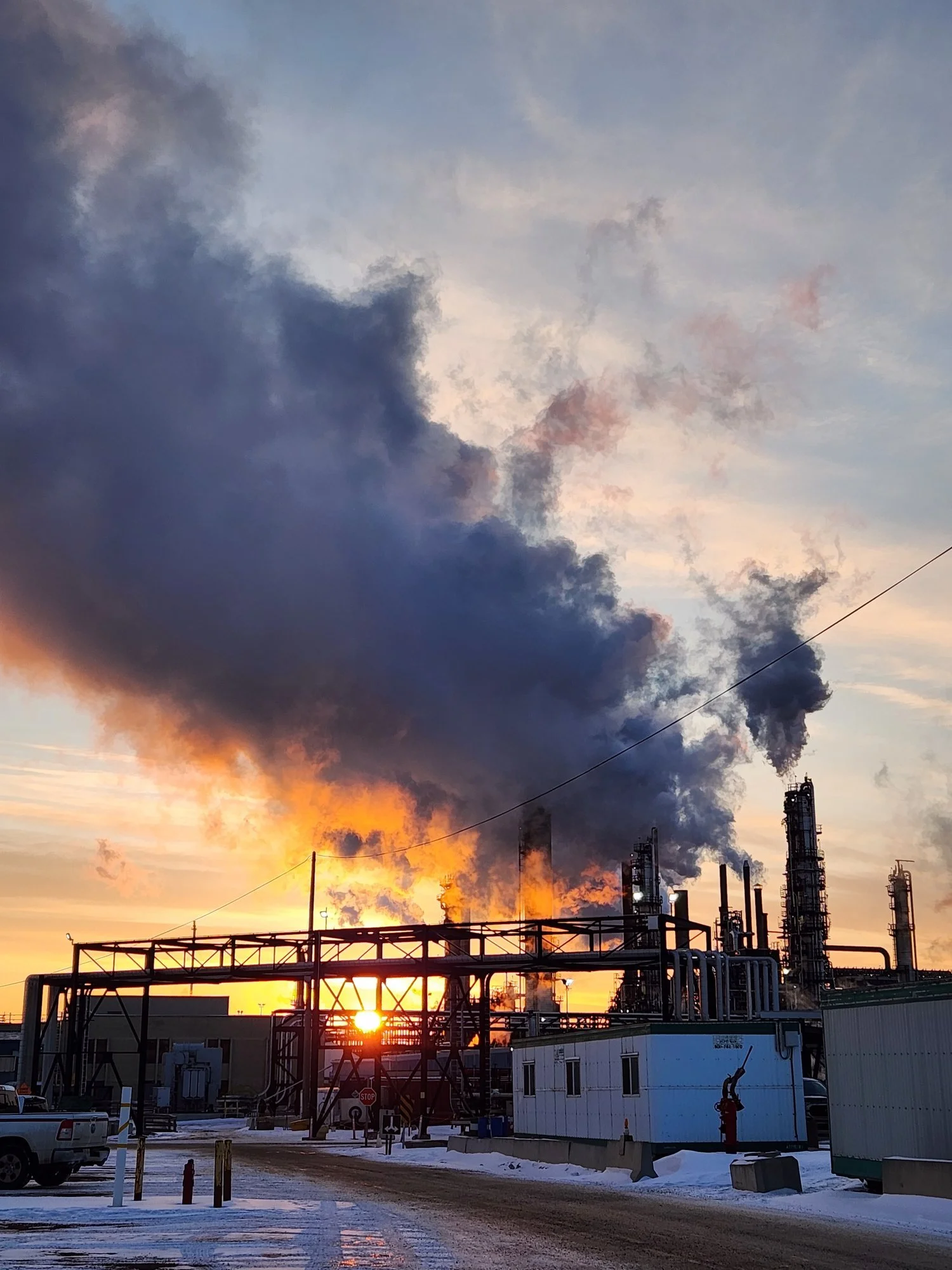 Oil and gas processing facility at sunrise with active steam stacks, illustrating industrial operations, compliance, and asset integrity in cold conditions.