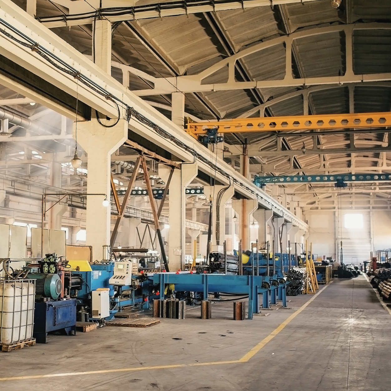 Manufacturing facility floor with production equipment and overhead cranes, supporting quality management and process control.