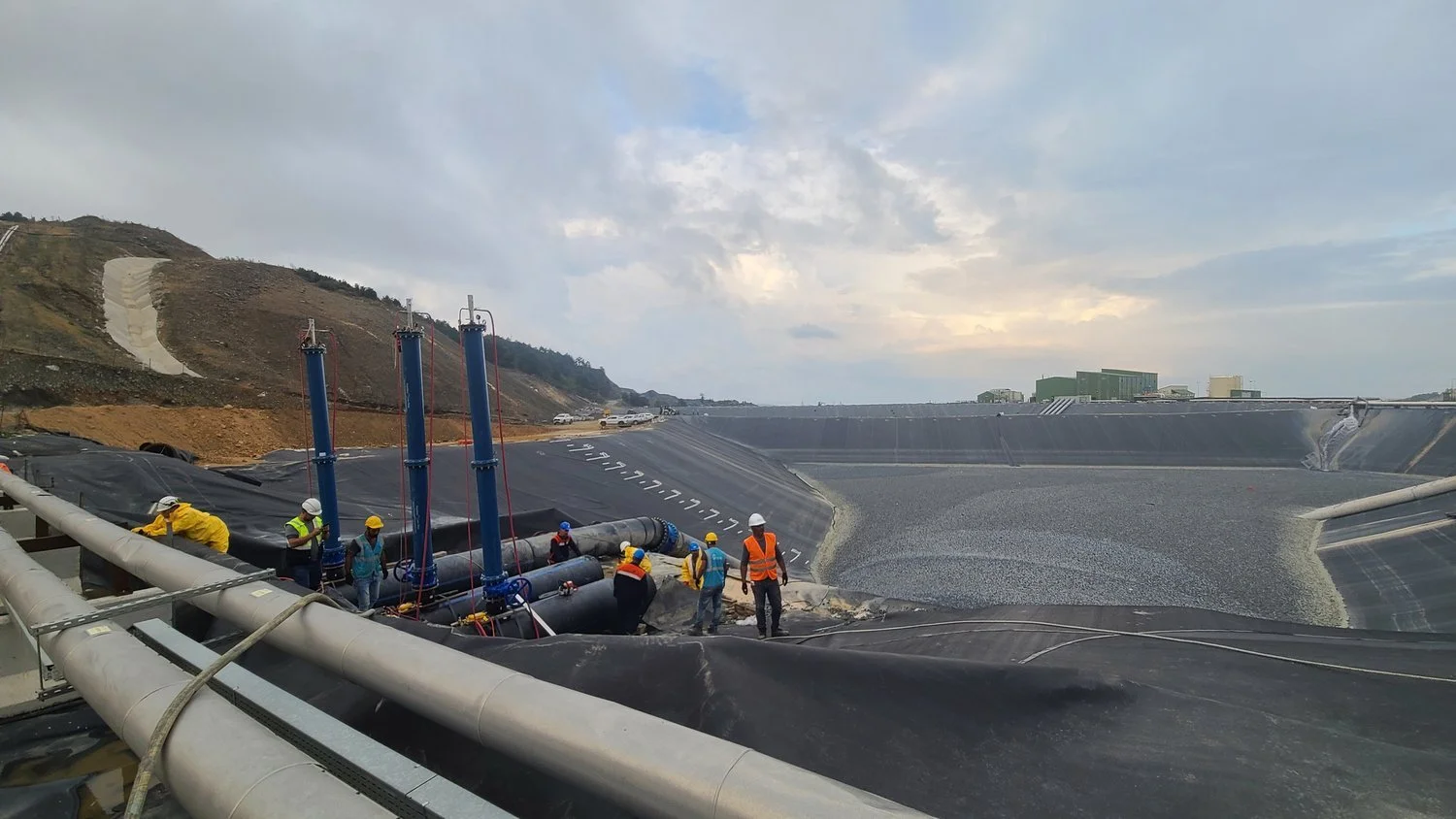 Mining facility containment area with large-diameter piping and crew performing installation work, highlighting construction oversight and quality control in extractive operations.