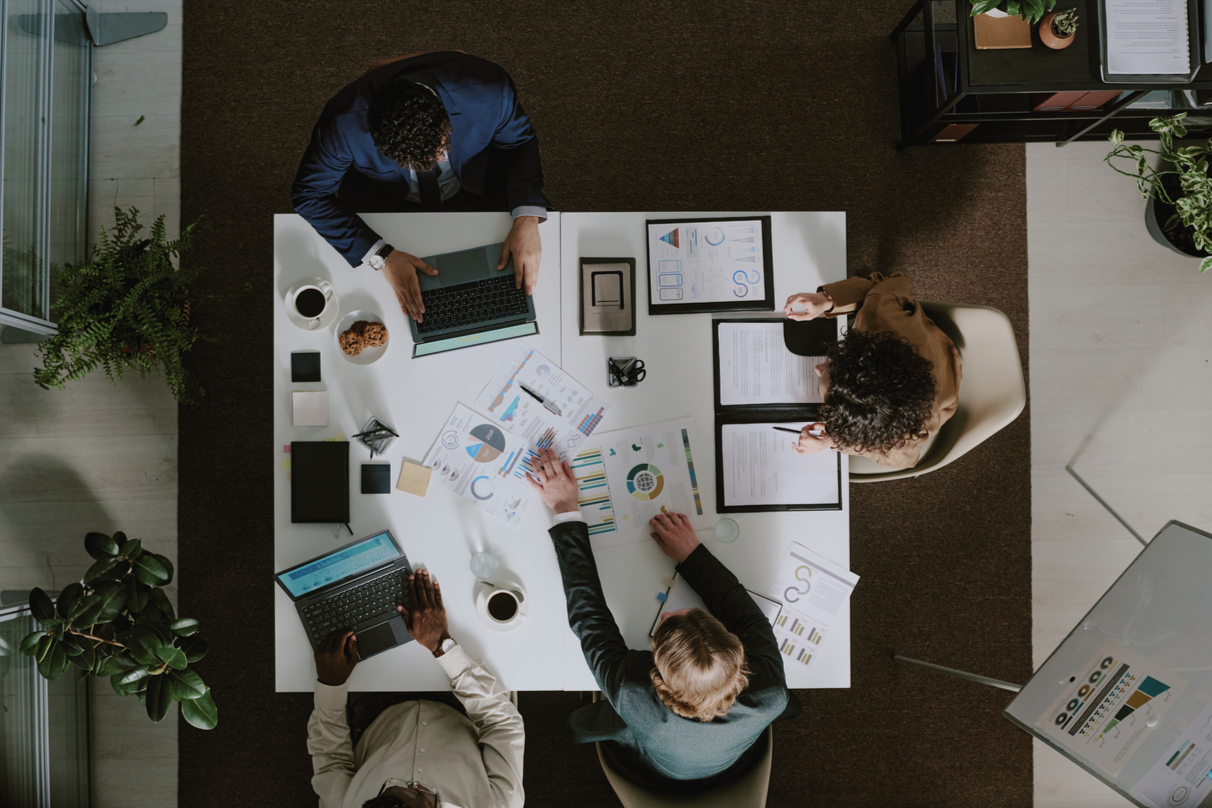 Team collaborating around a table reviewing quality plans, metrics, and documentation, representing shared visibility and strategic quality oversight.