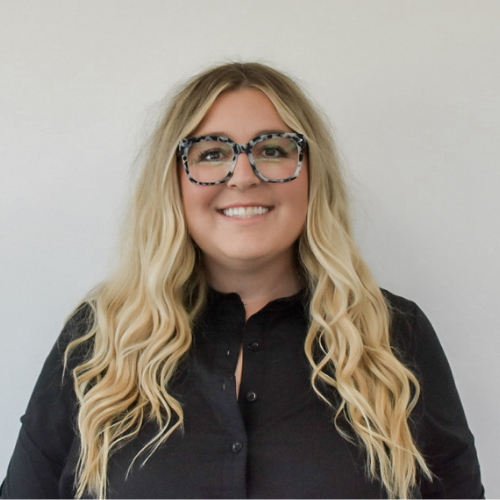 Professional headshot of a director of technology specializing in scalable quality management systems, wearing glasses and a black blouse against a neutral background.