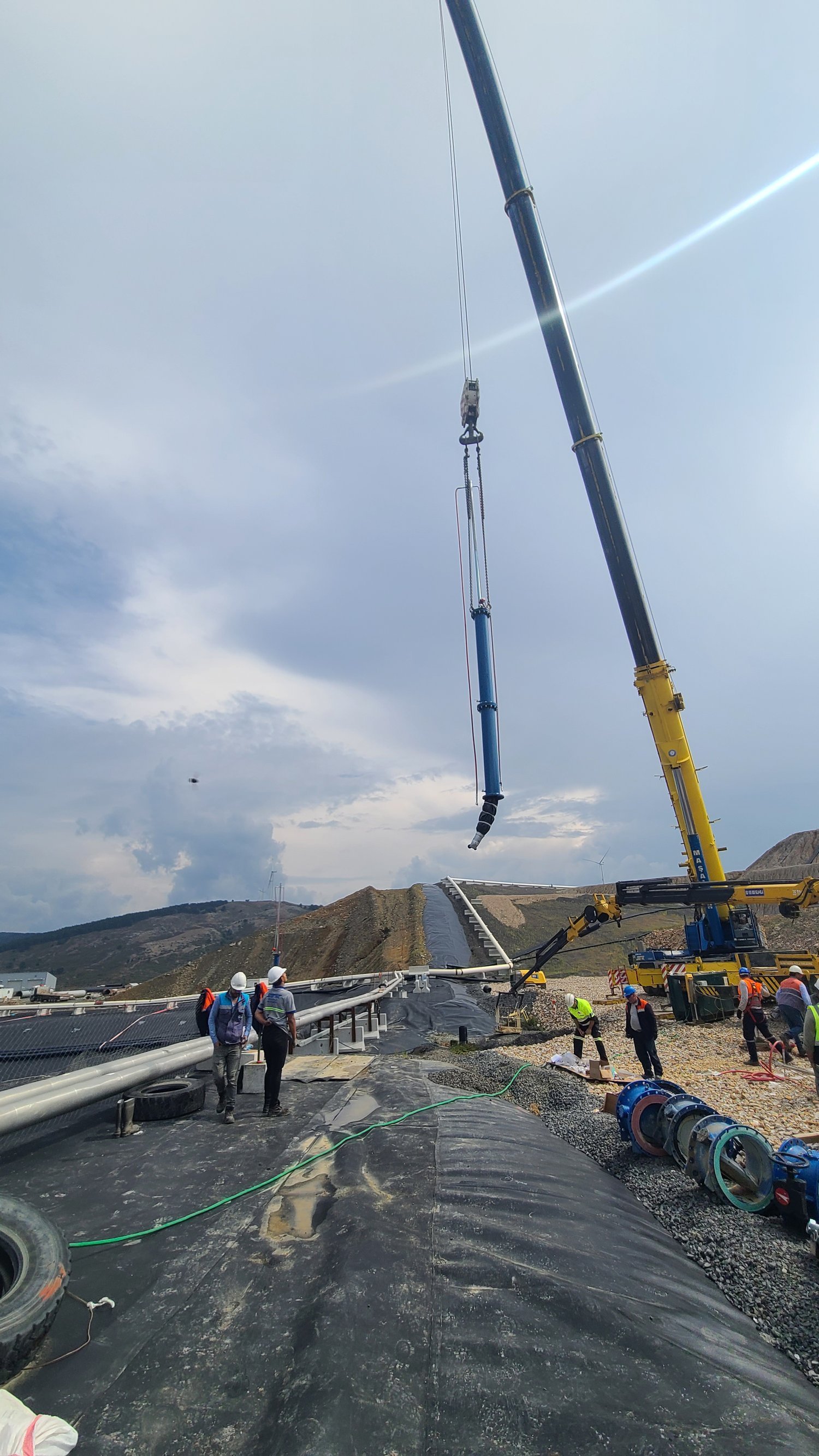 Crane lifting and positioning large pipeline components at a mining site, demonstrating controlled lifting operations, installation sequencing, and inspection oversight.