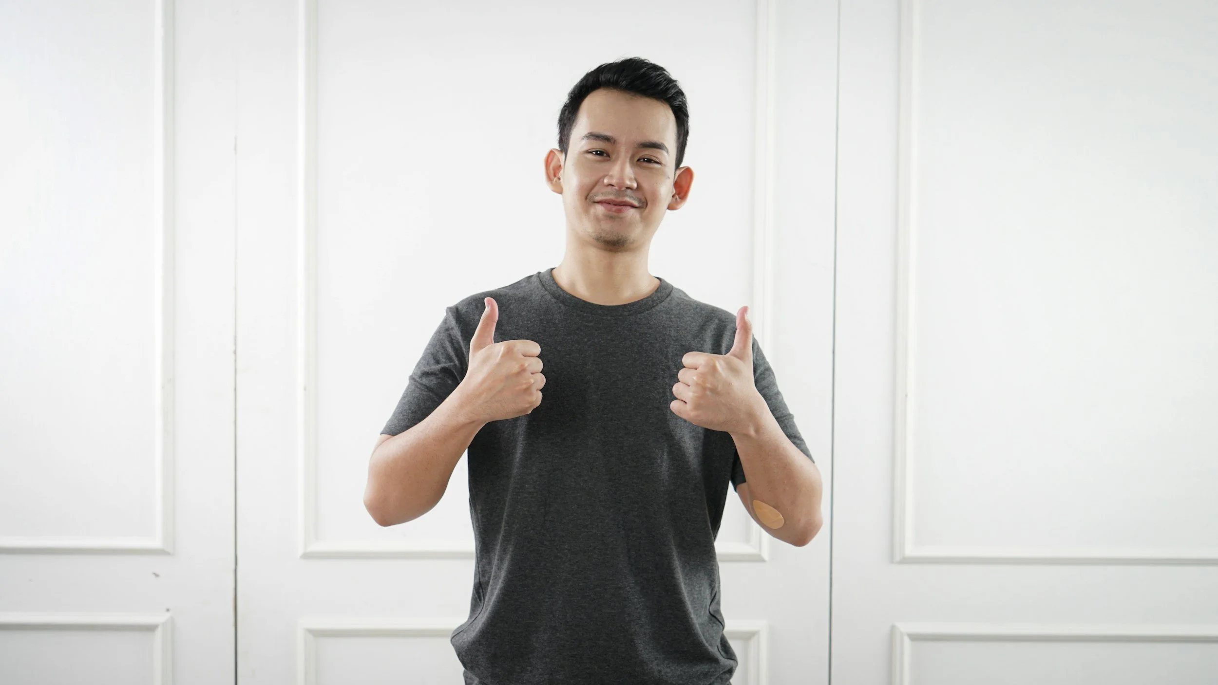 Asian Man, 20s to 30s, facing the camera, wearing a grey t-shirt, smiling and giving two thumbs up