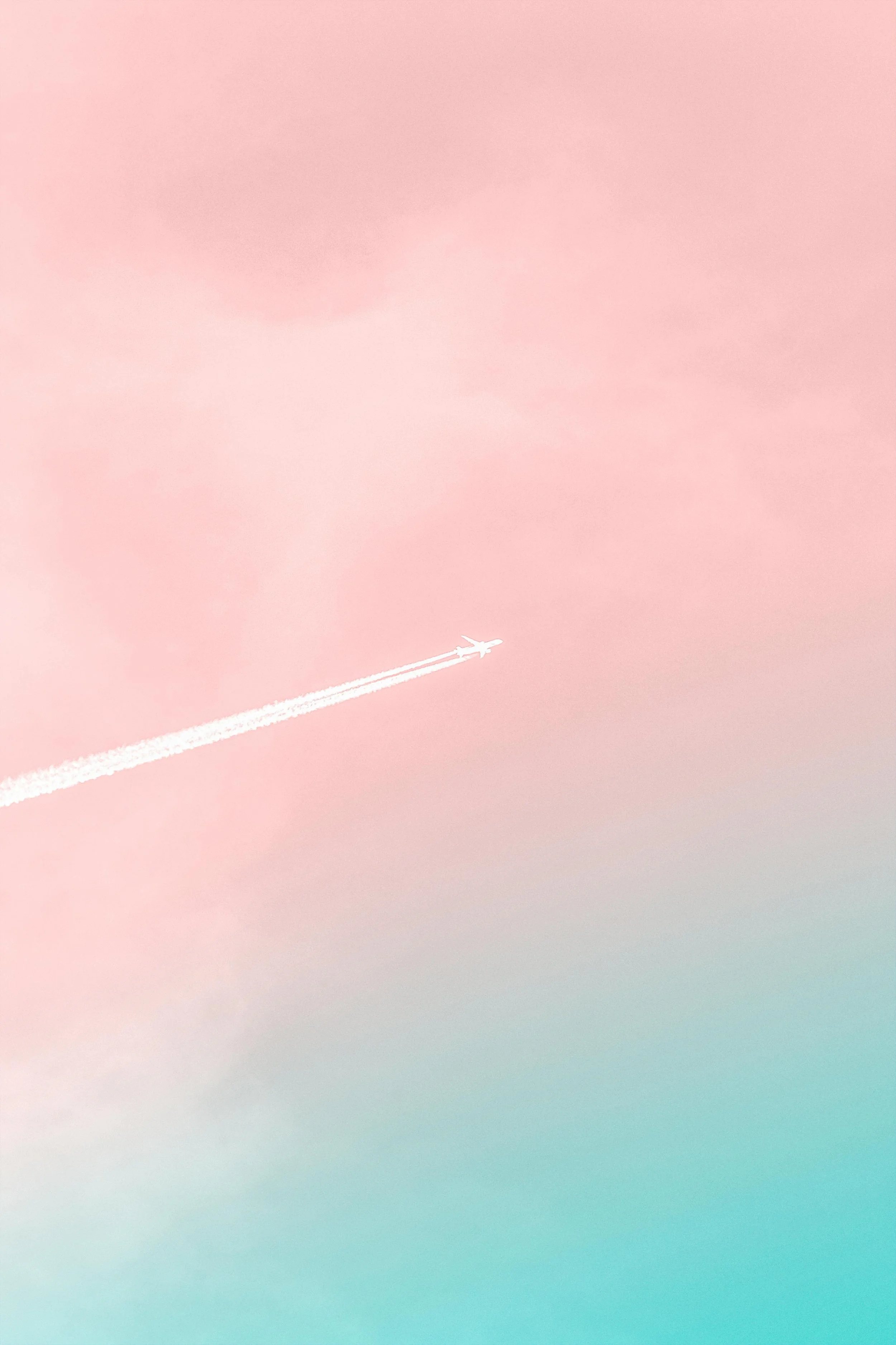 Airplane with contrail against a pink and blue sky