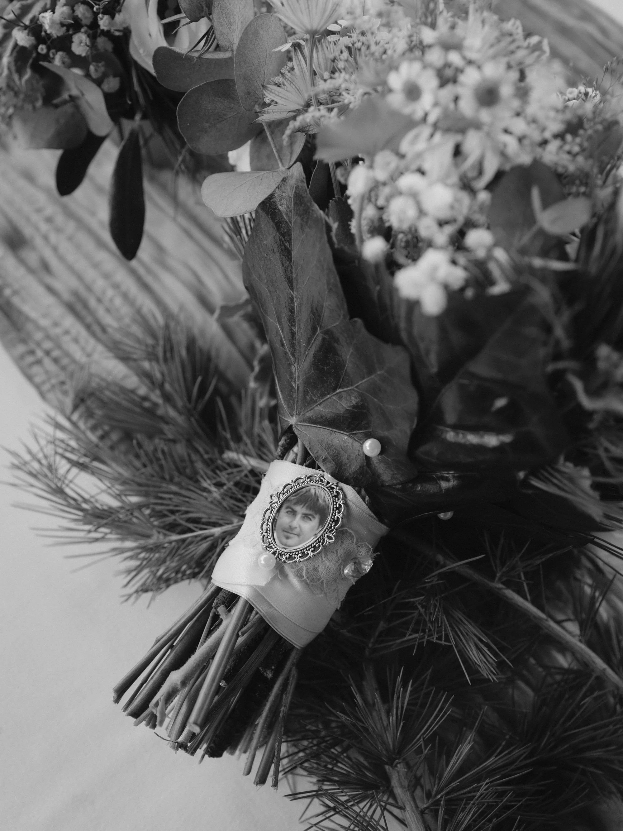 Ein Brautstrauß aus Blumen und grünen Blättern, mit einem kleinen Medaillon, das ein Portrait eines Mannes zeigt, dekoriert.