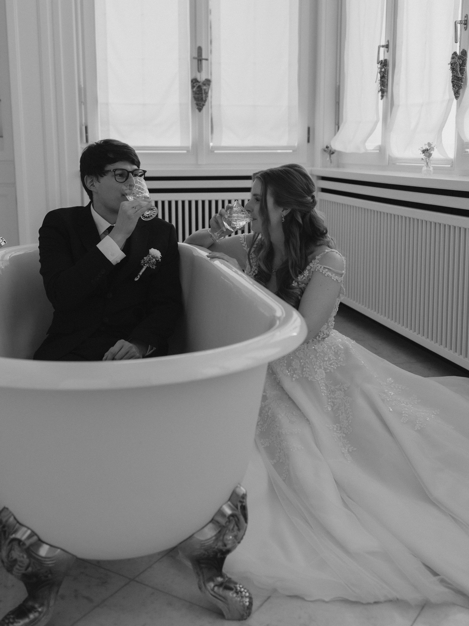 Ein Brautpaar in Hochzeitskleidung, das in einer Badewanne sitzt und auf Sektgläser anstößt. Hochzeit am Schluss Vasoldsberg.