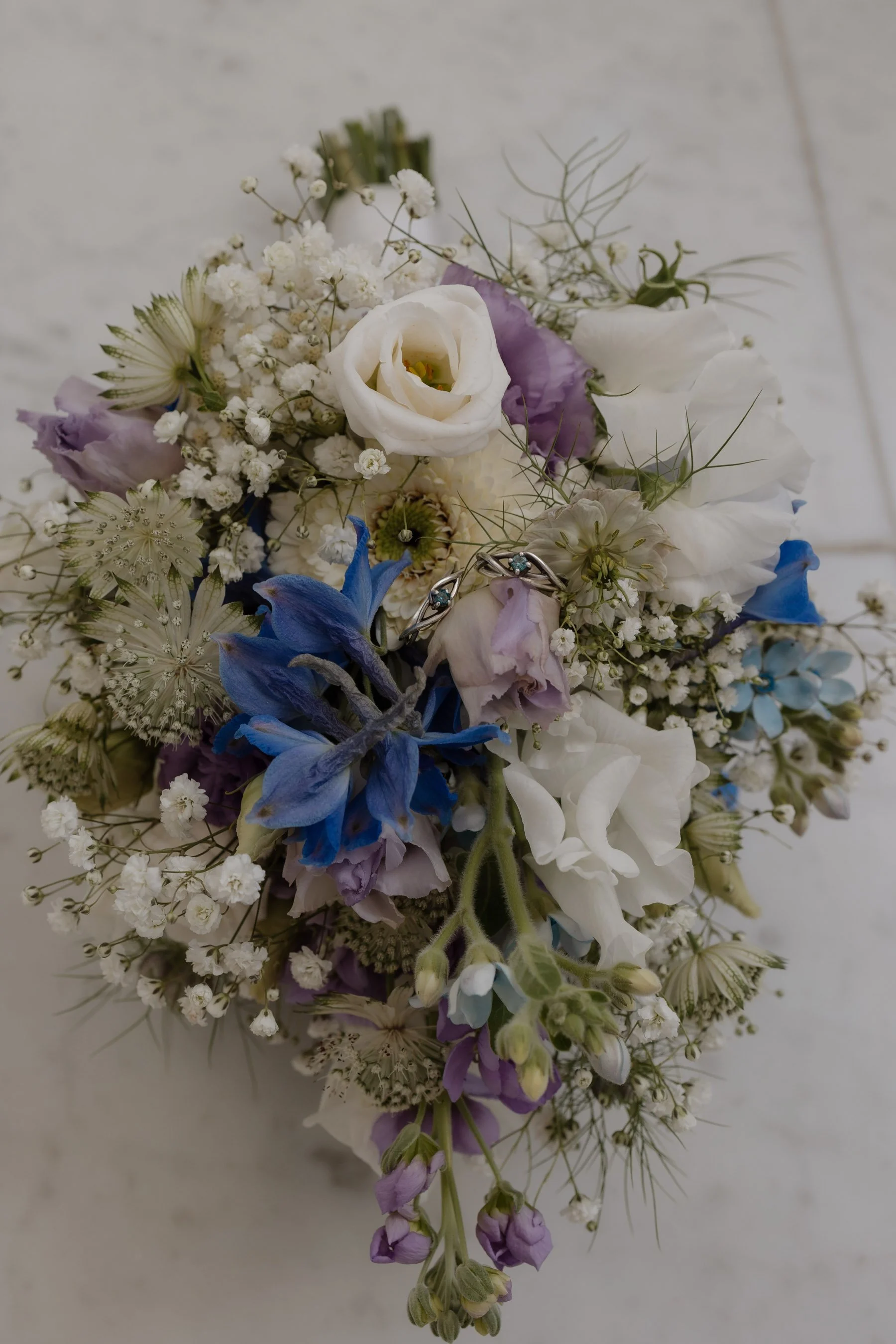 Blumenstrauß mit weißen, lilafarbenen, blauen und grünen Blumen, auf hellem Hintergrund.