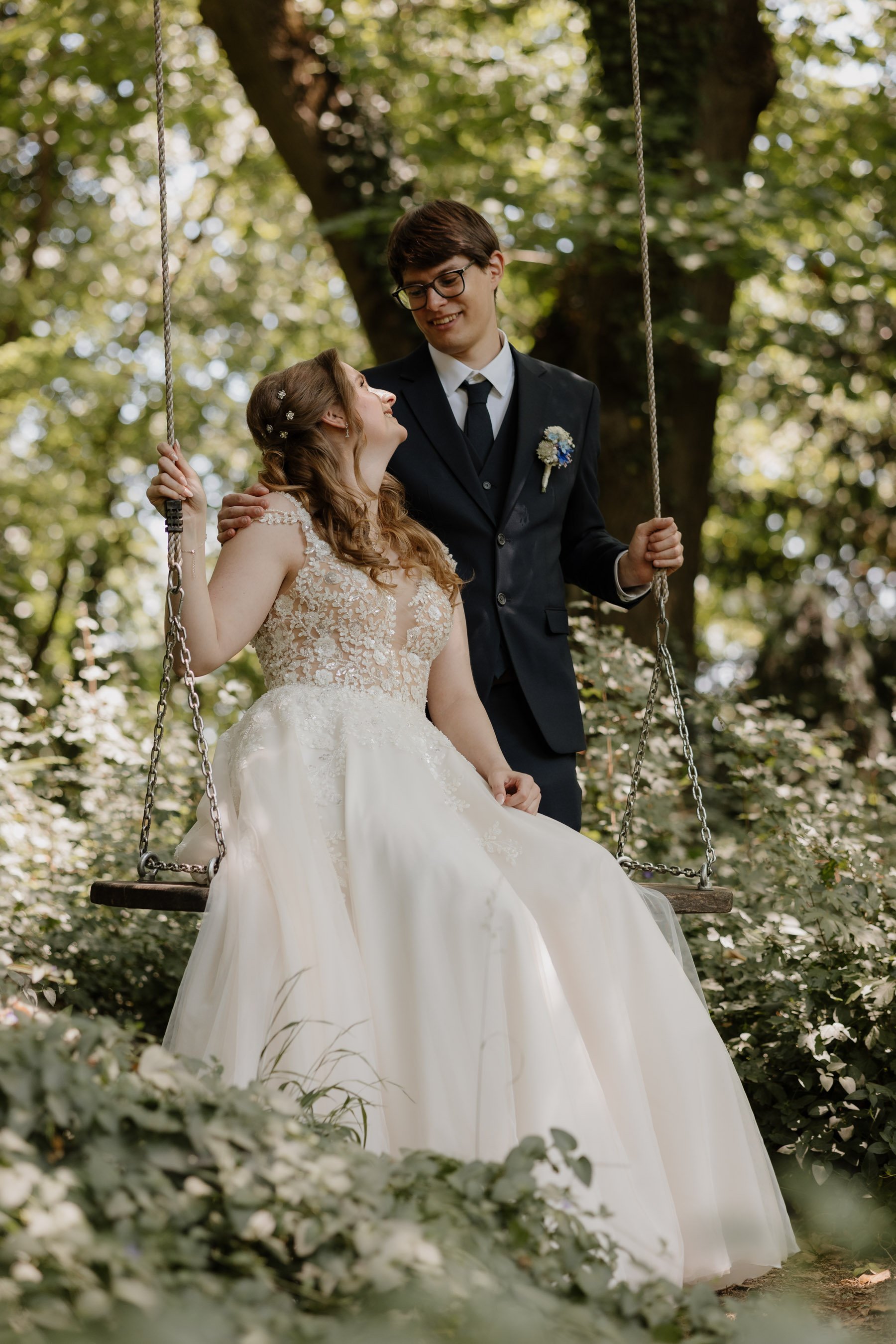 Braut und Bräutigam auf einem Baum-Schaukel im Wald, Hochzeit fotografiert, romantische Szenerie, naturell gemäßigt, Grün und braun Töne, fröhliche Atmosphäre. Im "Bridgerton" Stil Hochzeitsfotos, Steiermark, Kärnten. 