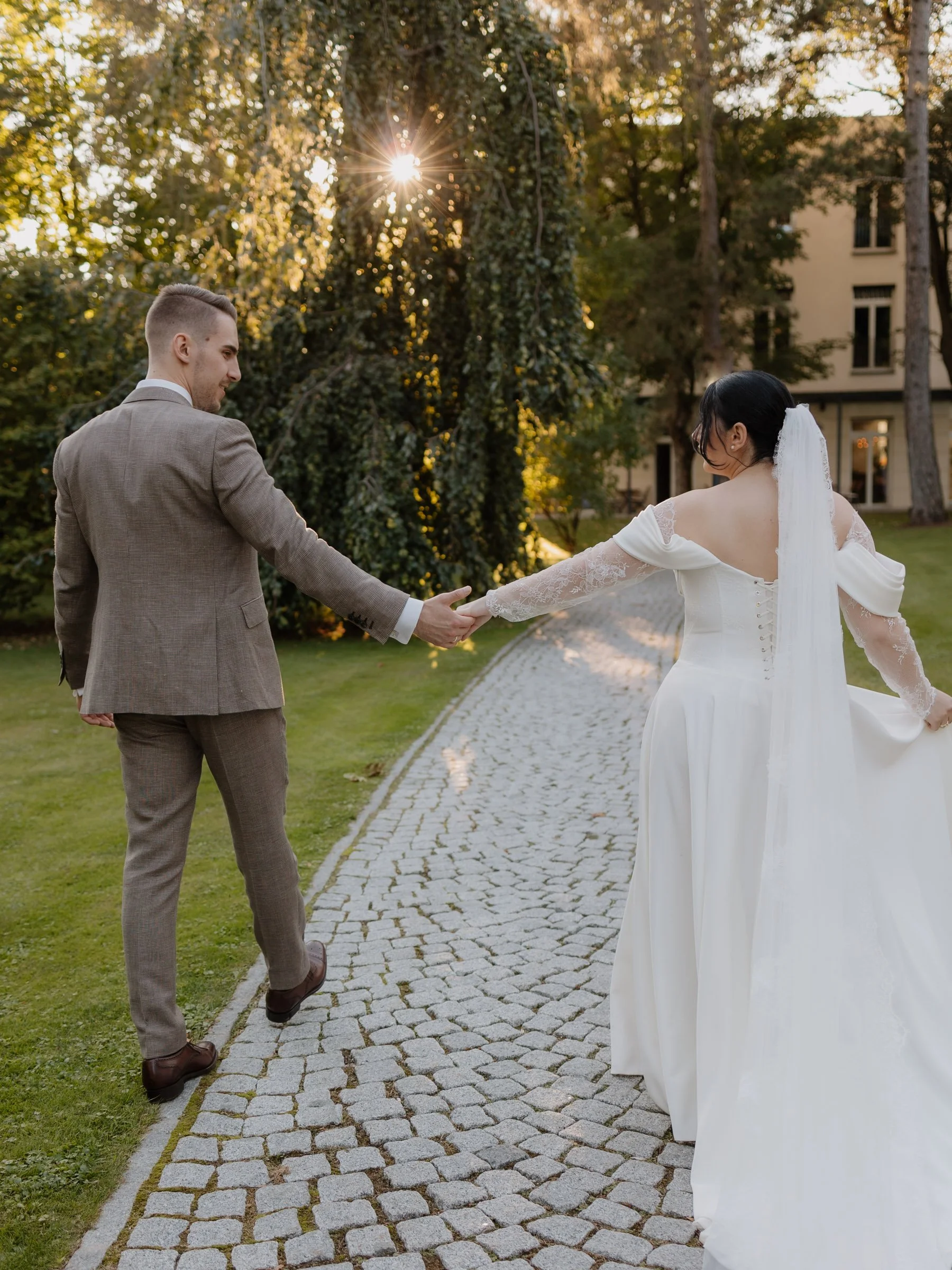 Ein Brautpaar tanzt im Garten bei Sonnenuntergang, die Frau trägt ein weißes Hochzeitskleid mit Schleier, der Mann trägt einen braunen Anzug.