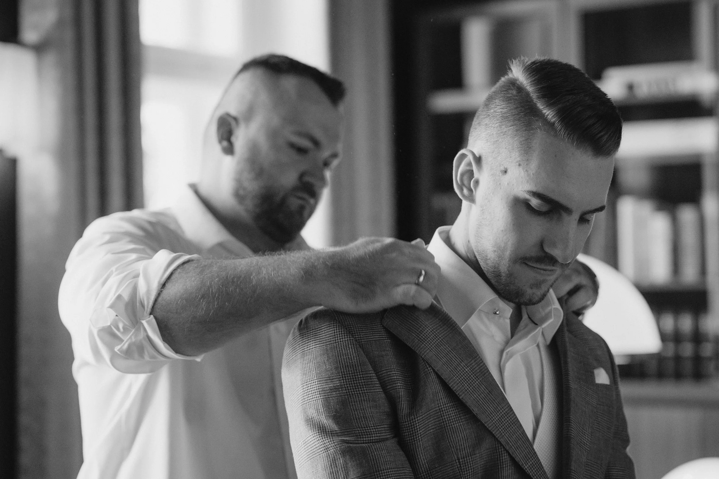 Getting Ready. Männer Getting Ready. Zwei Männer bei einer Besprechung, einer legt seine Hand auf die Schulter des anderen, im Hintergrund Bücherregale, schwarz-weiße Aufnahme.