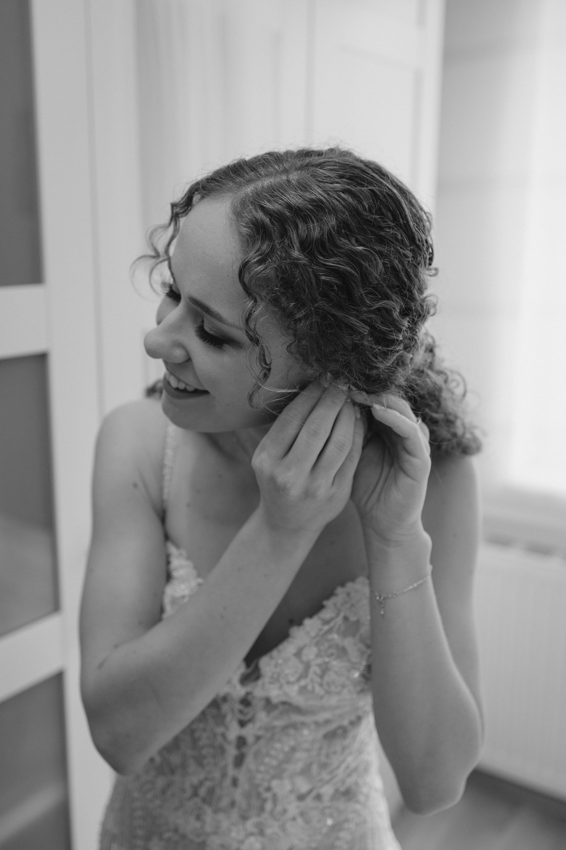 Schwarz-weiß-Foto einer lächelnden jungen Frau in Hochzeitskleid, die sich an den Ringfinger fasst, während sie nach unten schaut.