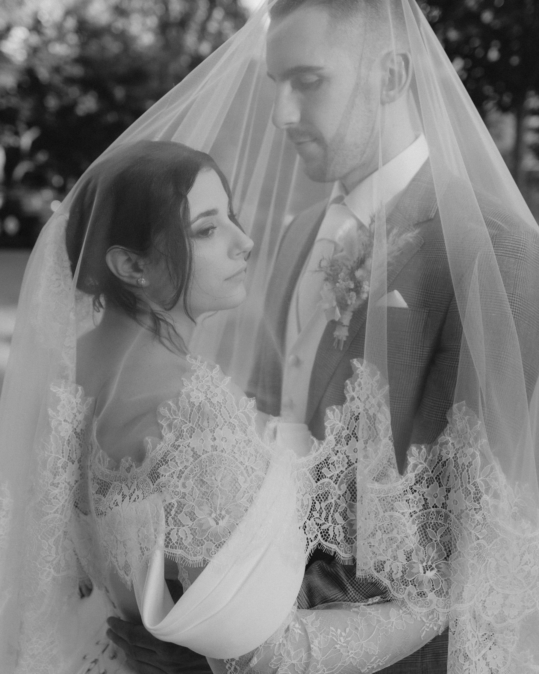 Paar bei ihrer Hochzeit, verhüllt mit einem Schleier, in schwarz-weiß. Die Frau trägt eine Brautkleid und der Mann trägt einen Anzug.