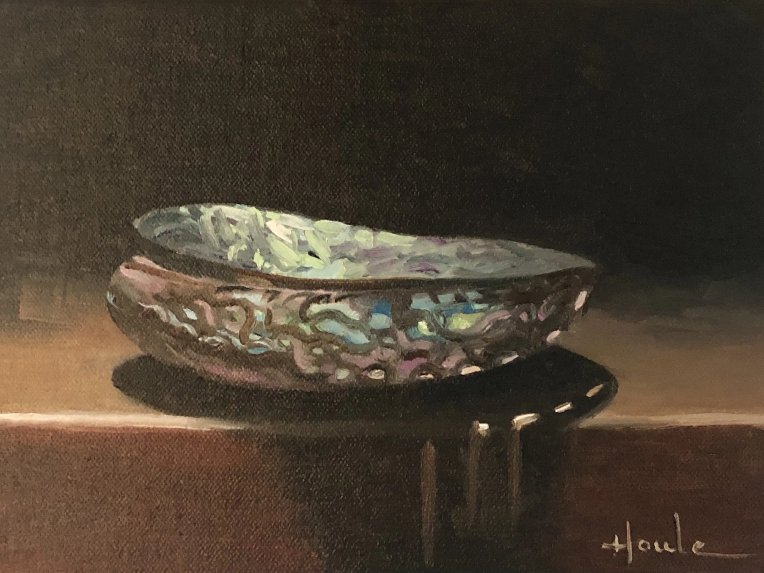 An iridescent abalone shell with multicolored highlights on a dark wood surface, with a dark background.