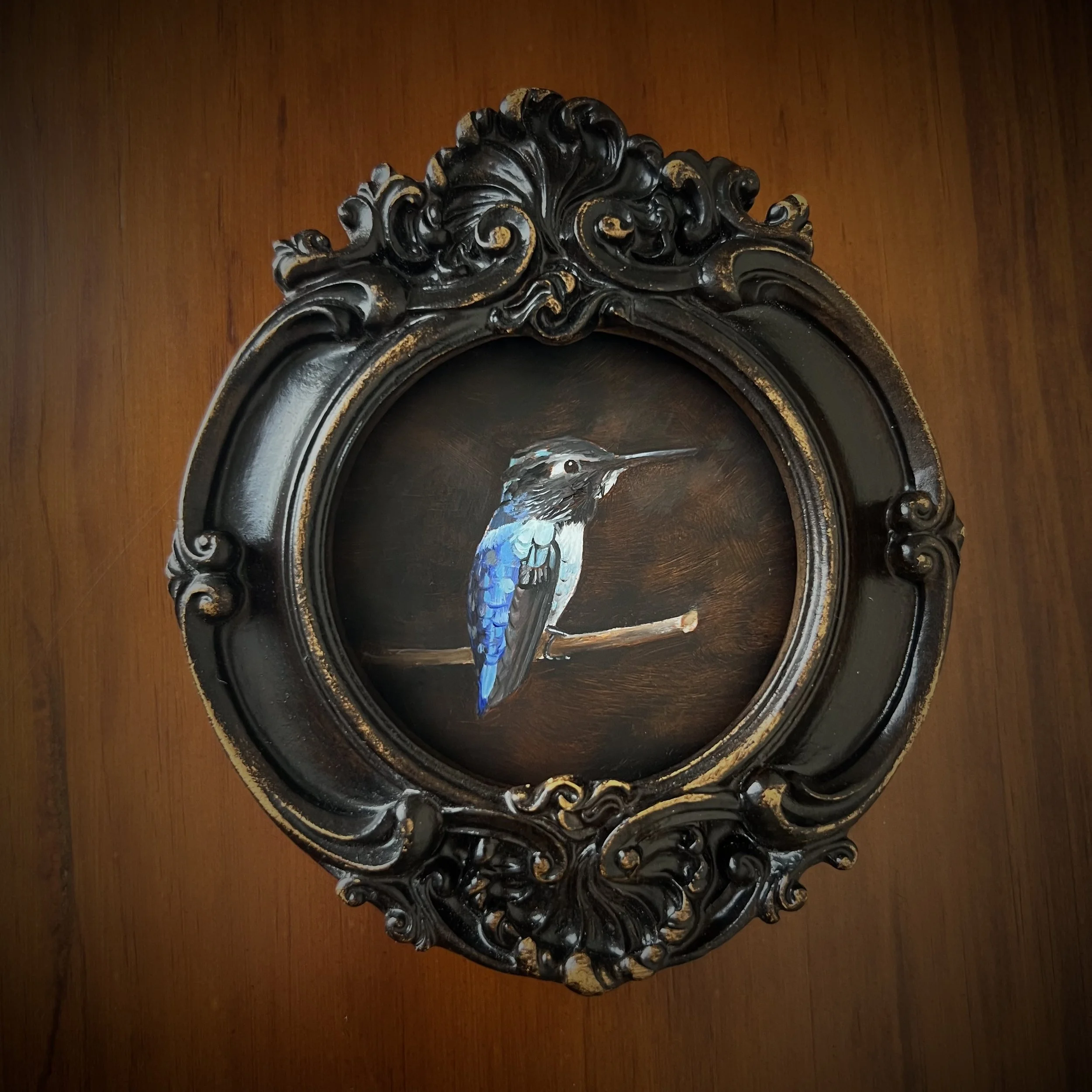Decorative vintage mirror with ornate black frame and a painted bird in the center, mounted on wooden wall.