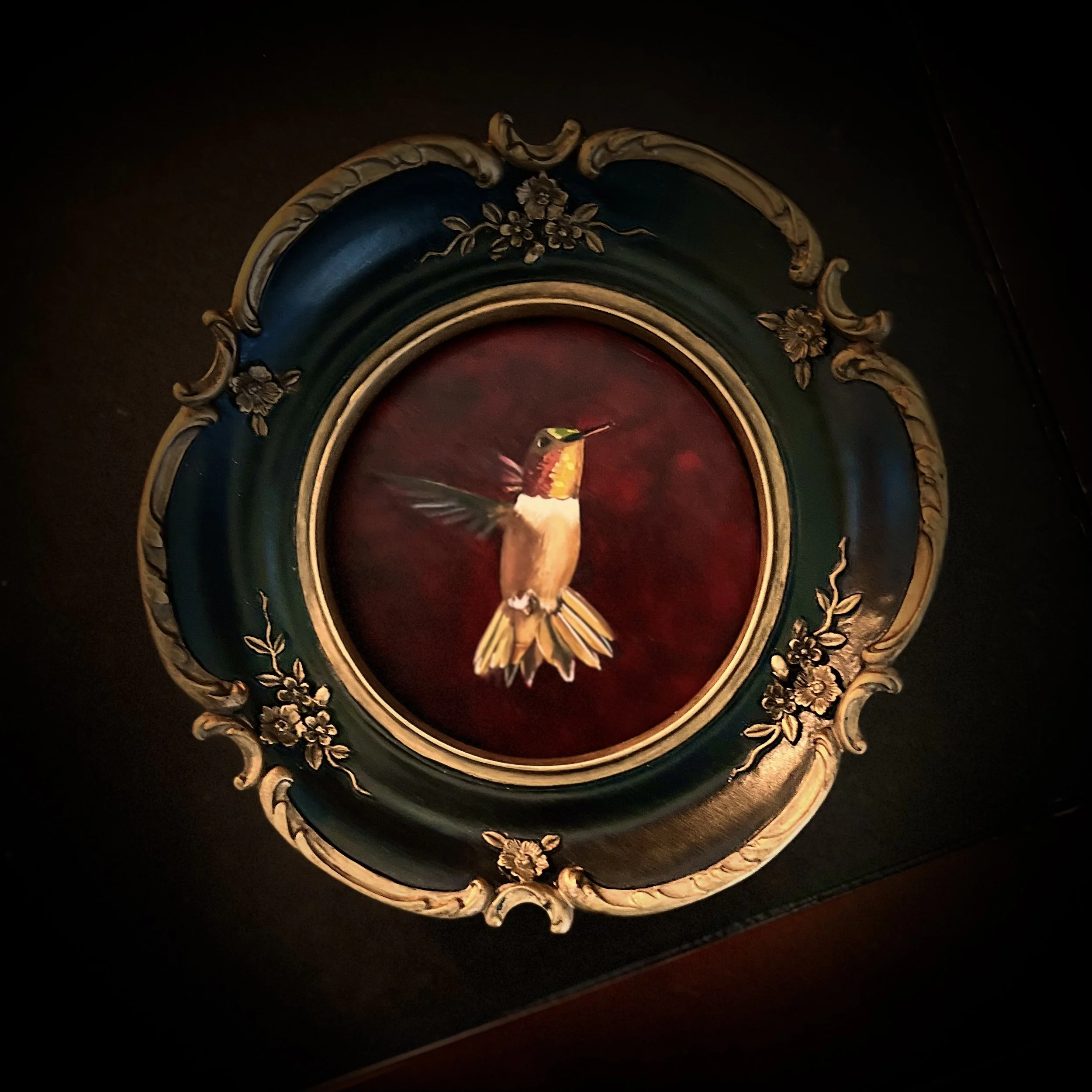 Ornate antique clock with a decorative frame featuring floral designs and gold accents, displaying a small bird figurine in the center.