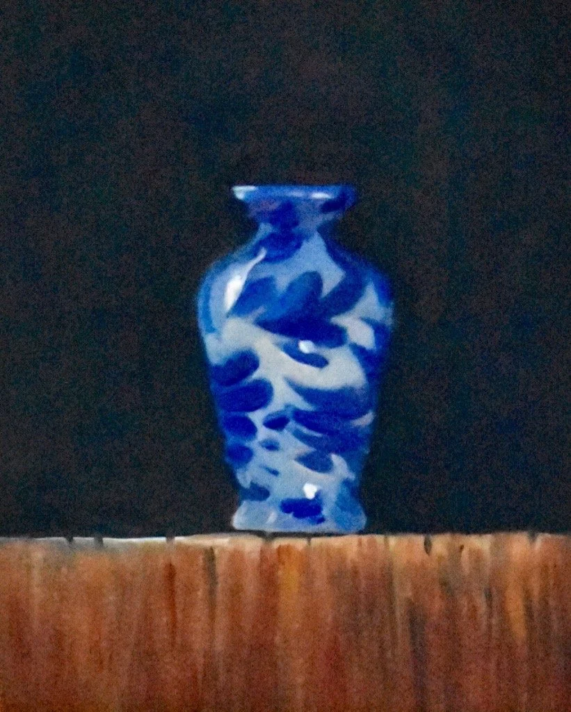 A blue-and-white ceramic vase with abstract patterns, placed on a wooden surface against a dark background.