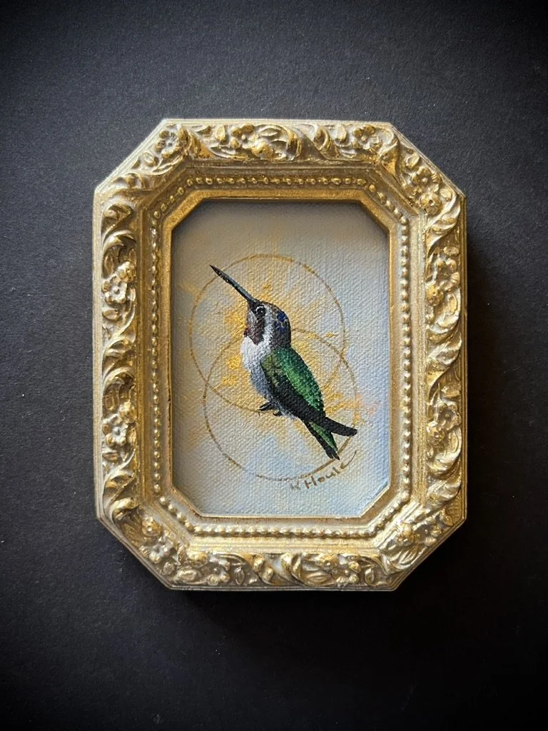 A small decorative picture frame with a painting of a hummingbird, featuring green and blue feathers, a long beak, and a yellow background with abstract design elements.