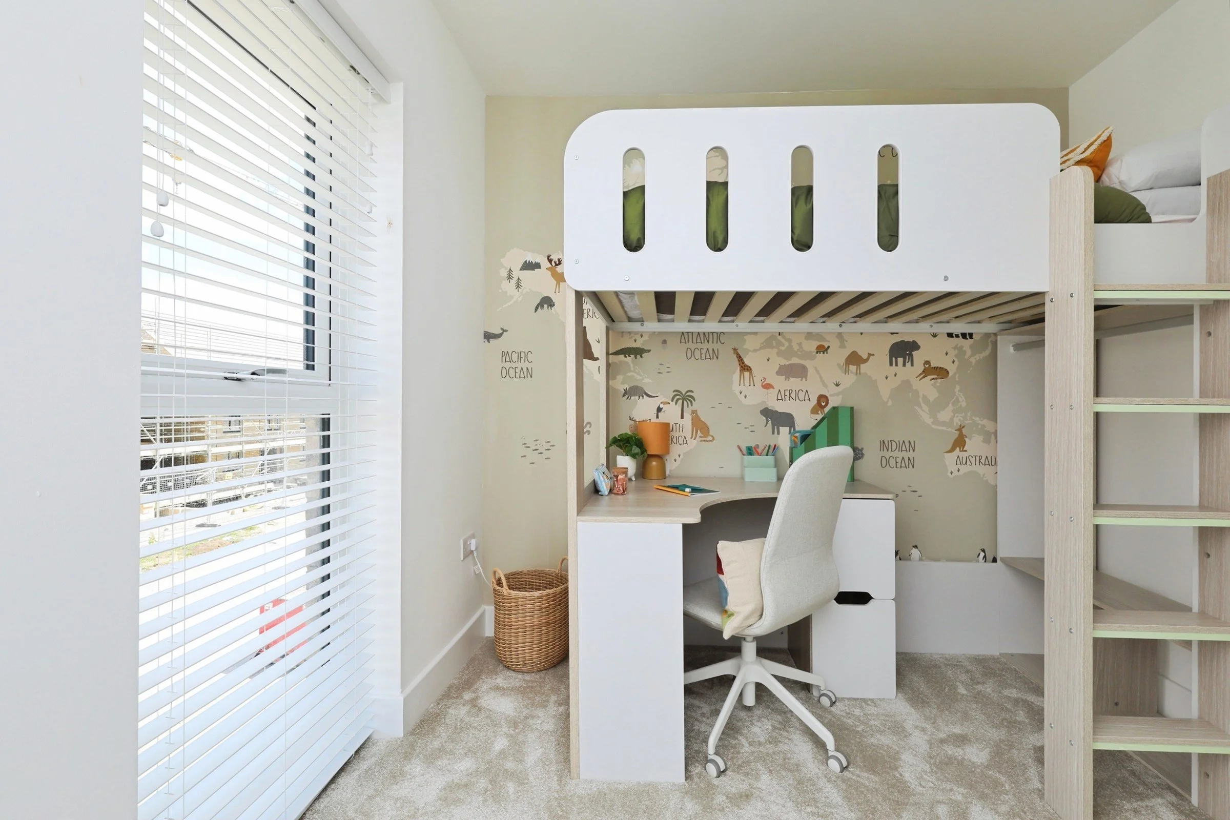 A children's bedroom with a loft bed, a desk beneath, a white swivel chair, a world map wall decal, window with blinds, and beige carpet.