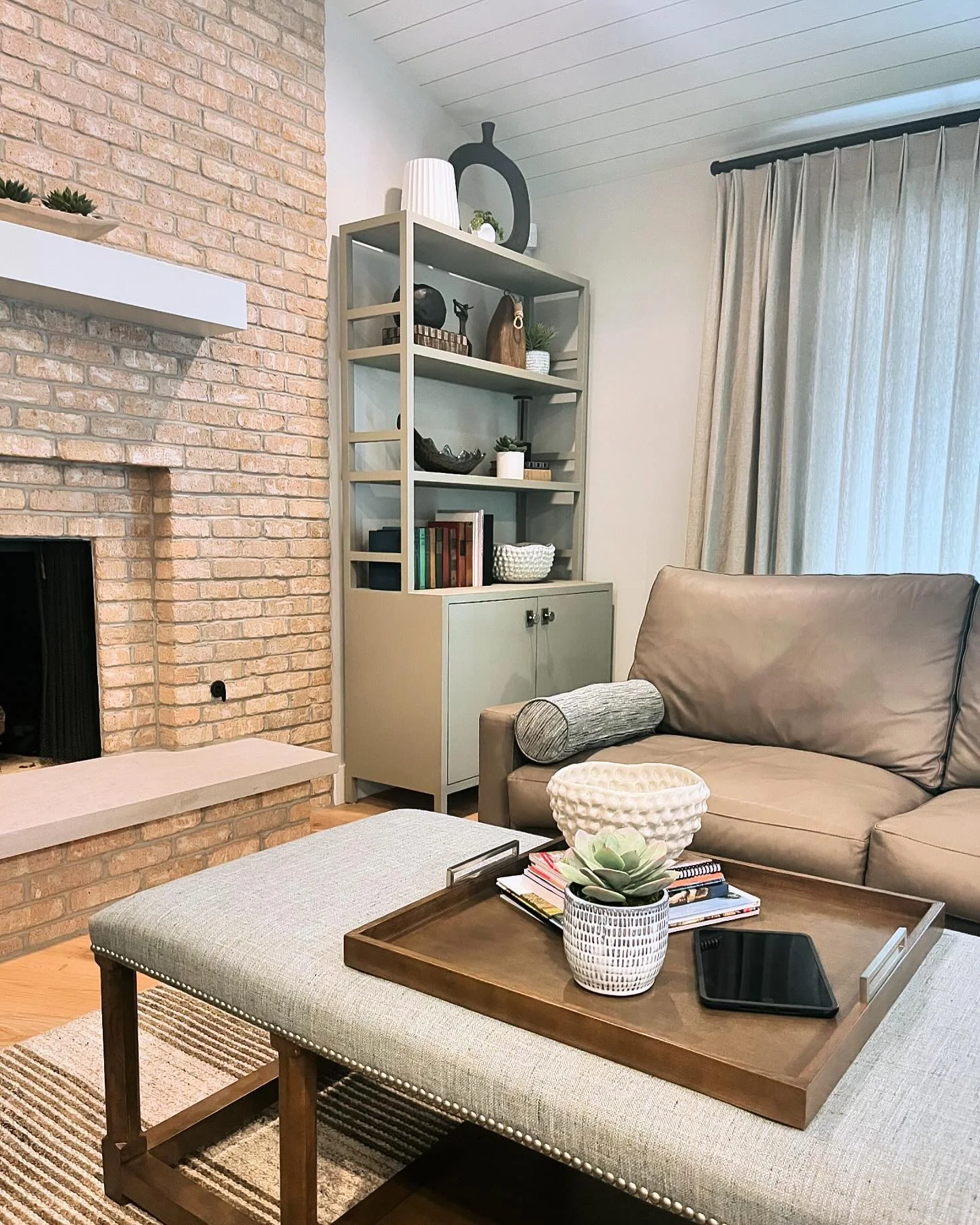We love blending texture and simplicity to create spaces that feel welcoming and sophisticated! 🌿 This living area showcases a perfect mix of modern accents and natural materials. The soft gray tones, warm brick fireplace, and elegant shelving displ