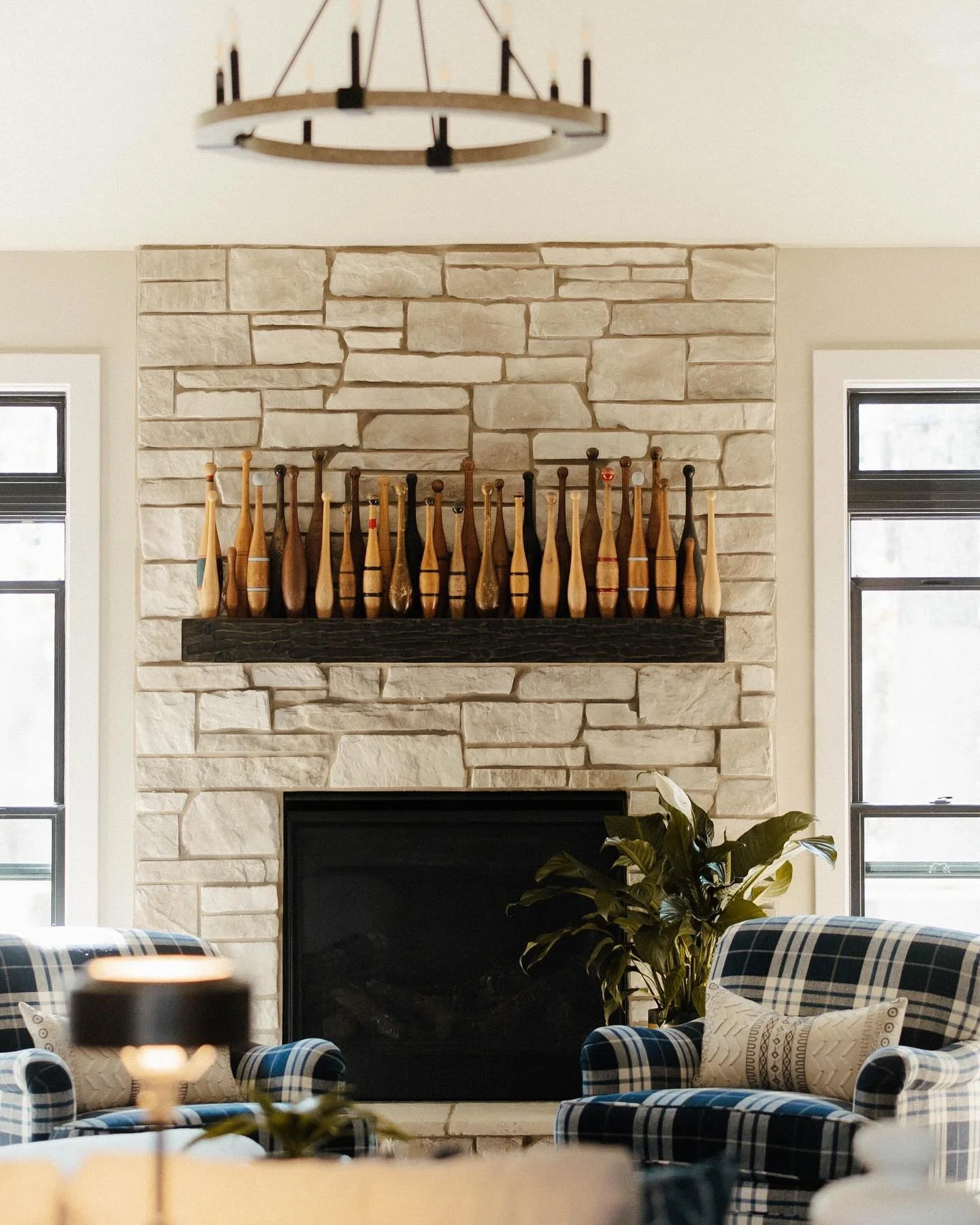 Loving the mix of textures and tones in this living space! The warm stone fireplace adds character, while the unique vintage-style collection above the mantel brings in a bit of whimsy. Paired with the modern plaid chairs and subtle greenery, this ro
