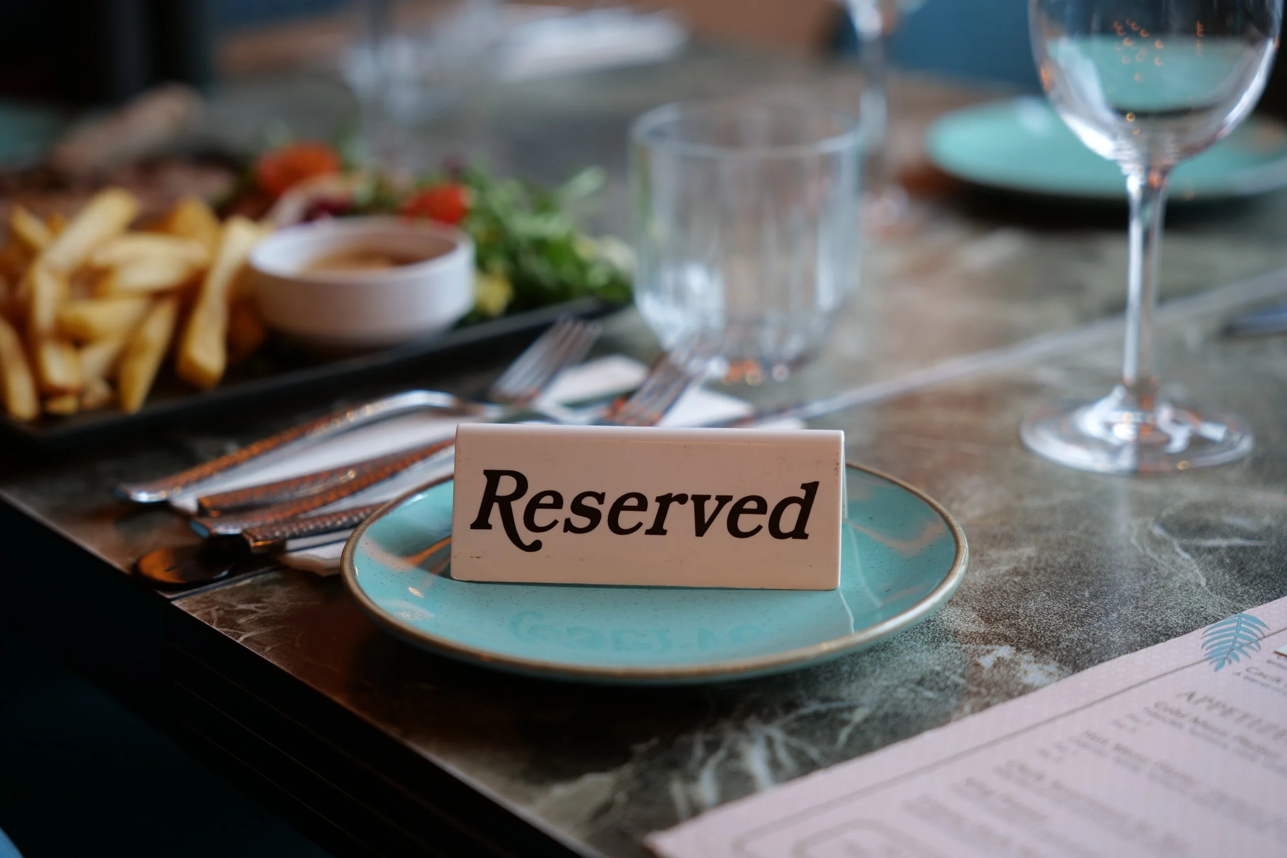 Photography restaurant content at a Bristol restaurant showing a table setting with a reserved sign on a turquoise plate, glasses, silverware, and a plate of French fries and salad in the background.