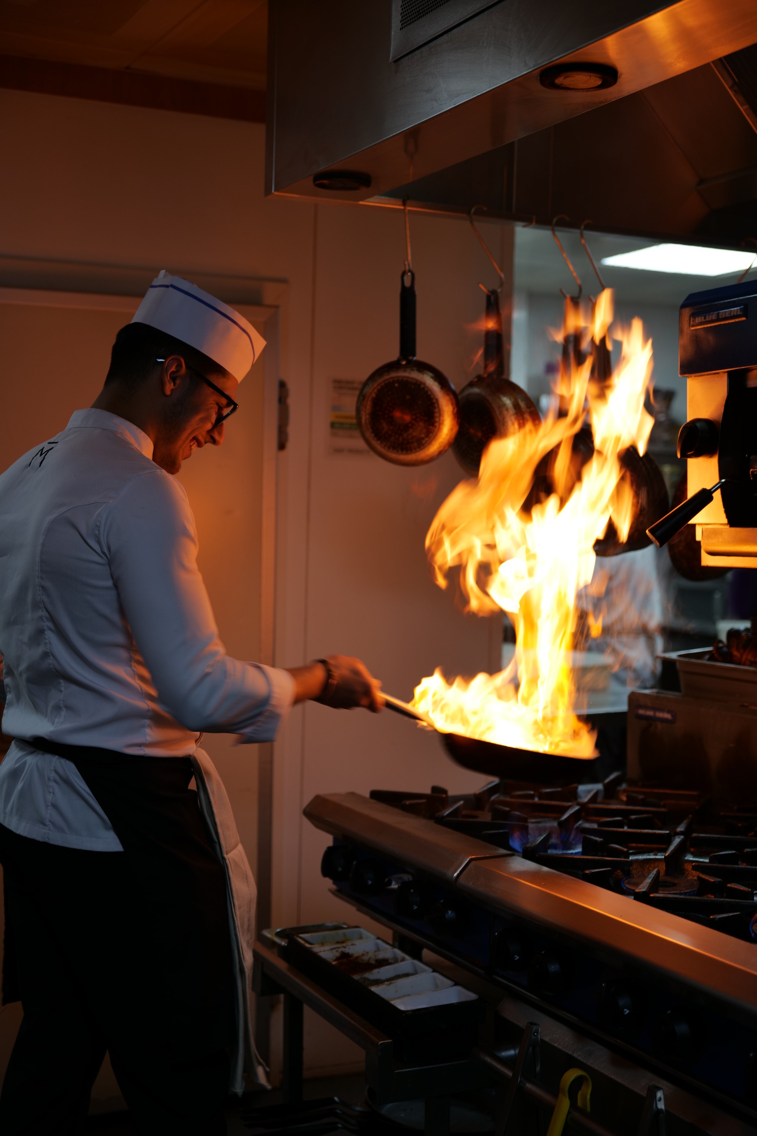 Photography restaurant content showing a chef cooking on a stove with large flames in a professional kitchen.