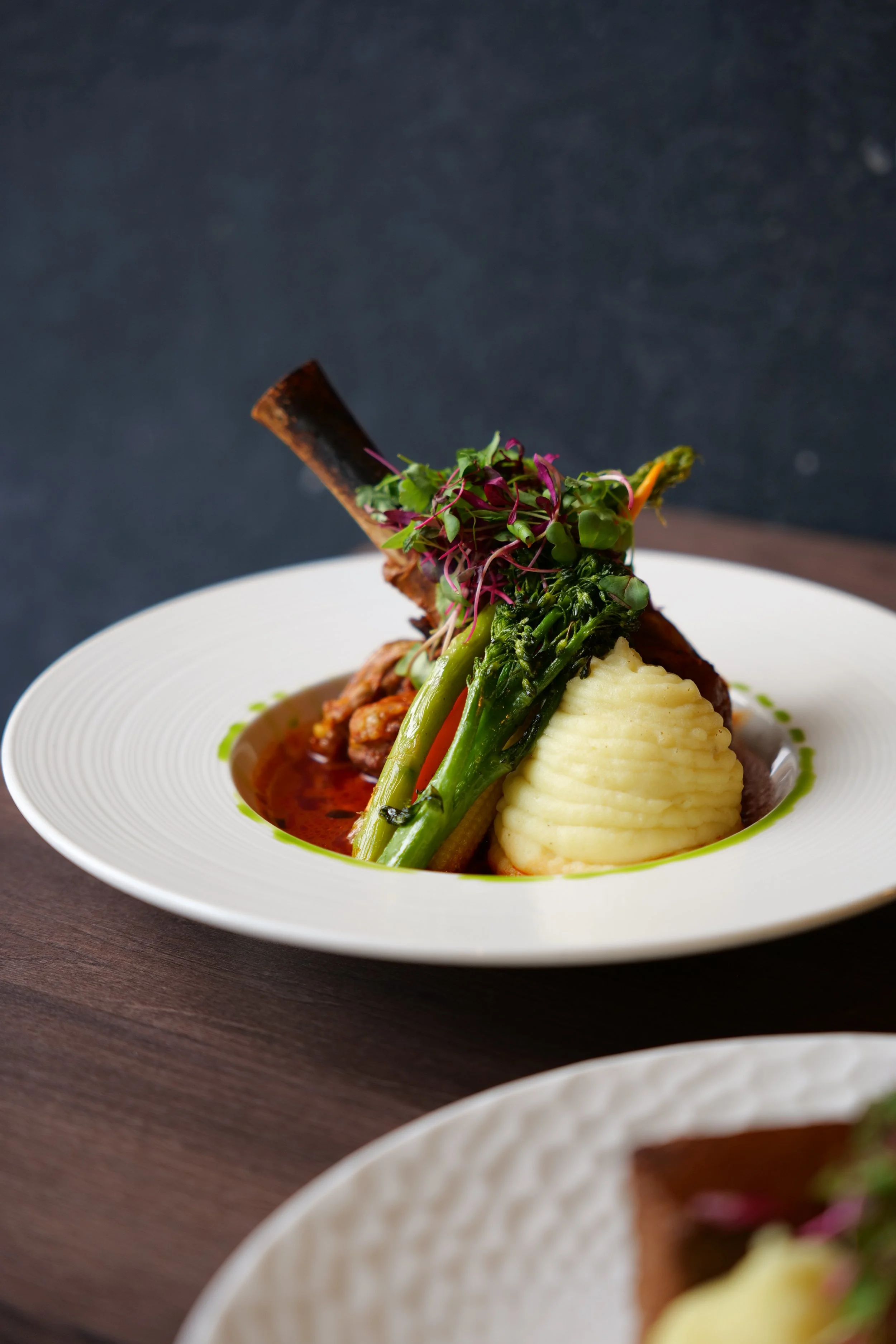 Photography restaurant content showing a plate of cooked lamb rack with mashed potatoes, grilled asparagus, and microgreens