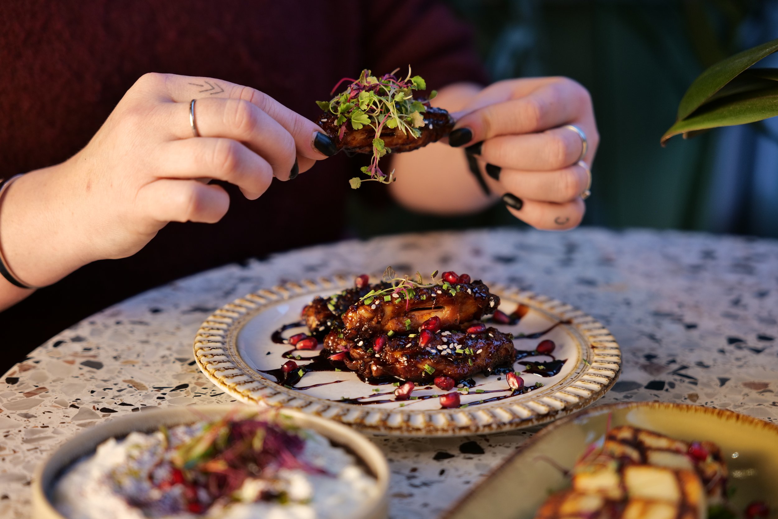 Photography restaurant content of a person decorating a dish with microgreens at a table with colourful plates of food and a granite surface.