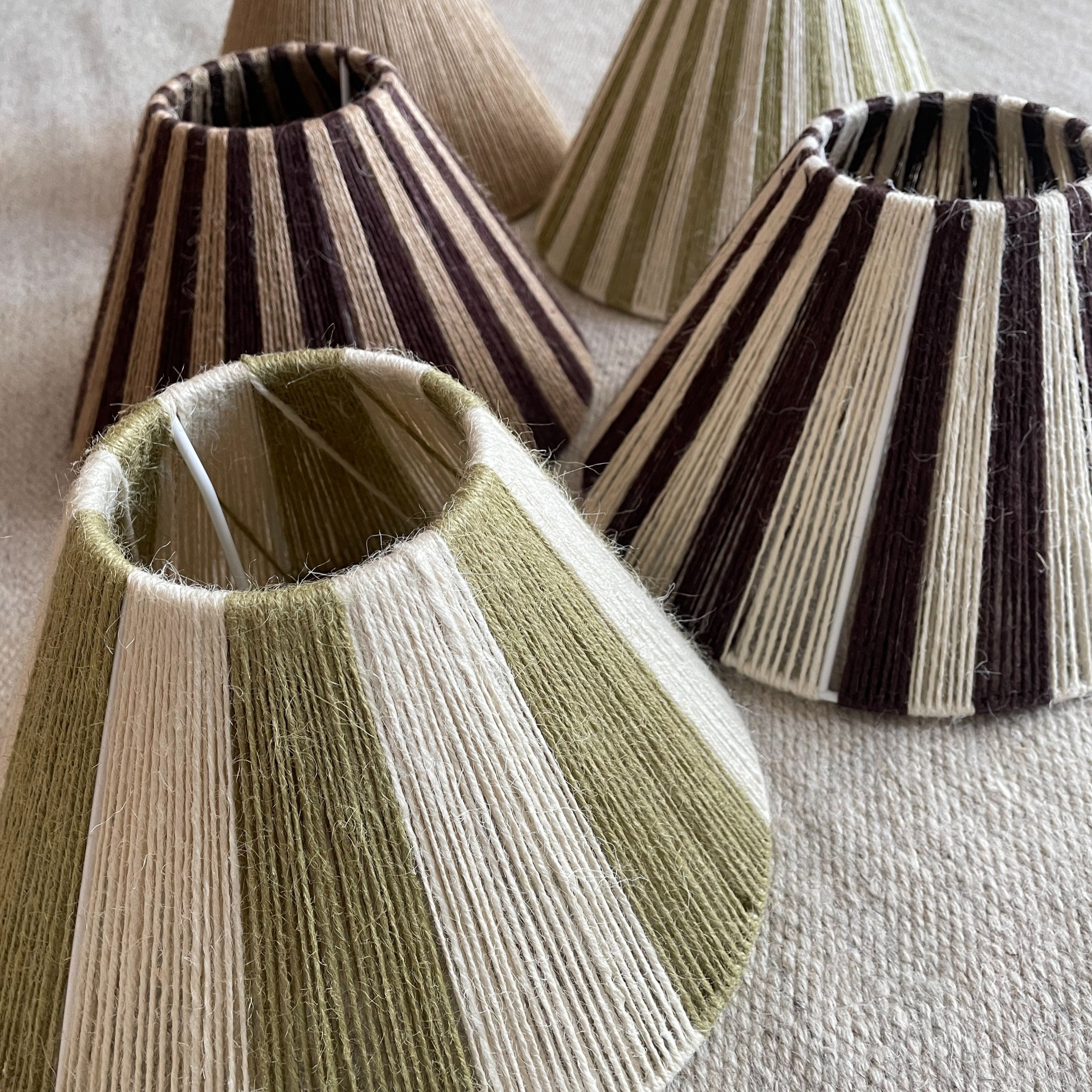 Assorted striped woven lampshades in green, beige, and brown hues on a fabric surface.