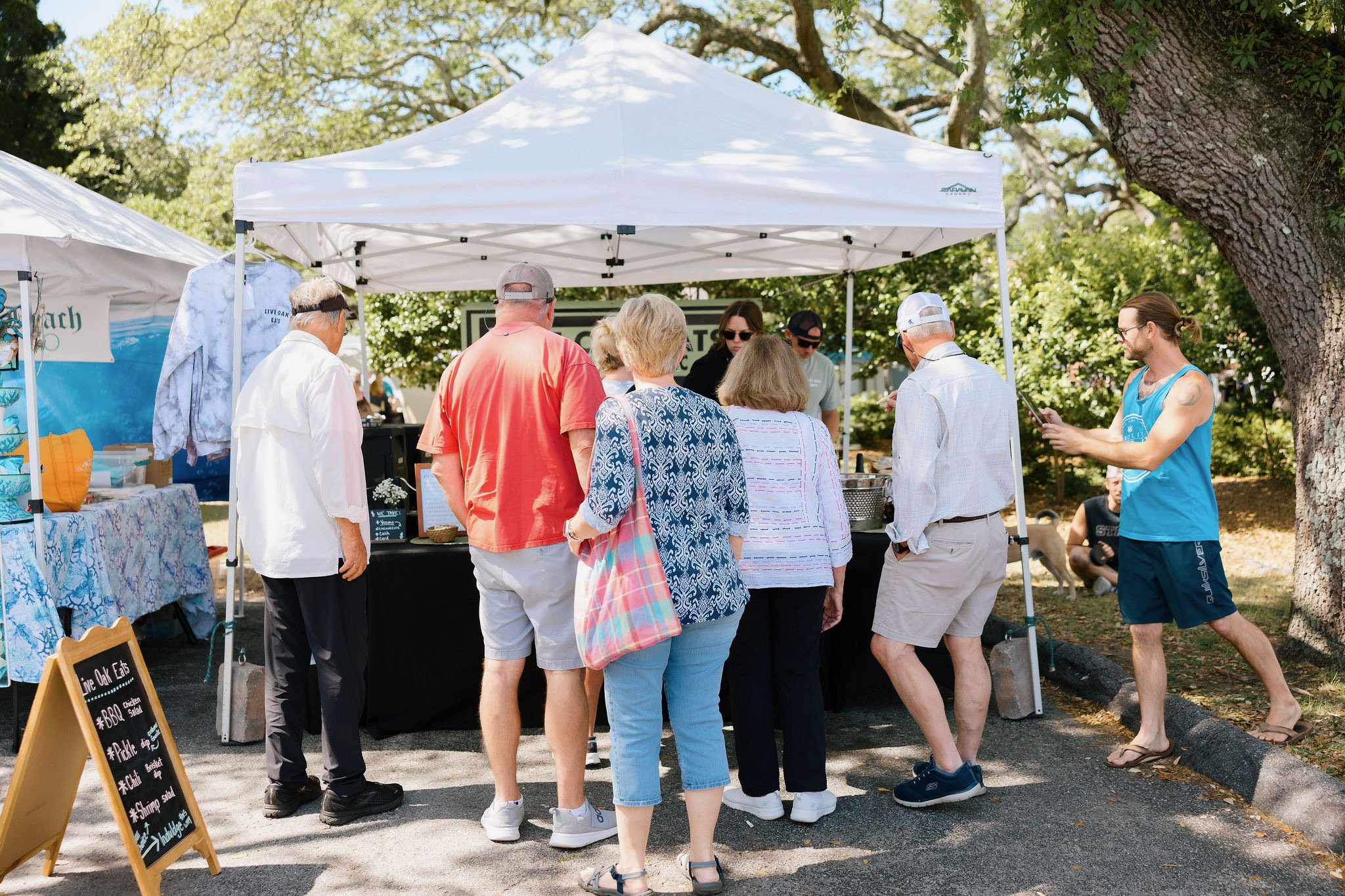 Farmers market setup with a crowd of people standing around a tent to buy items.
