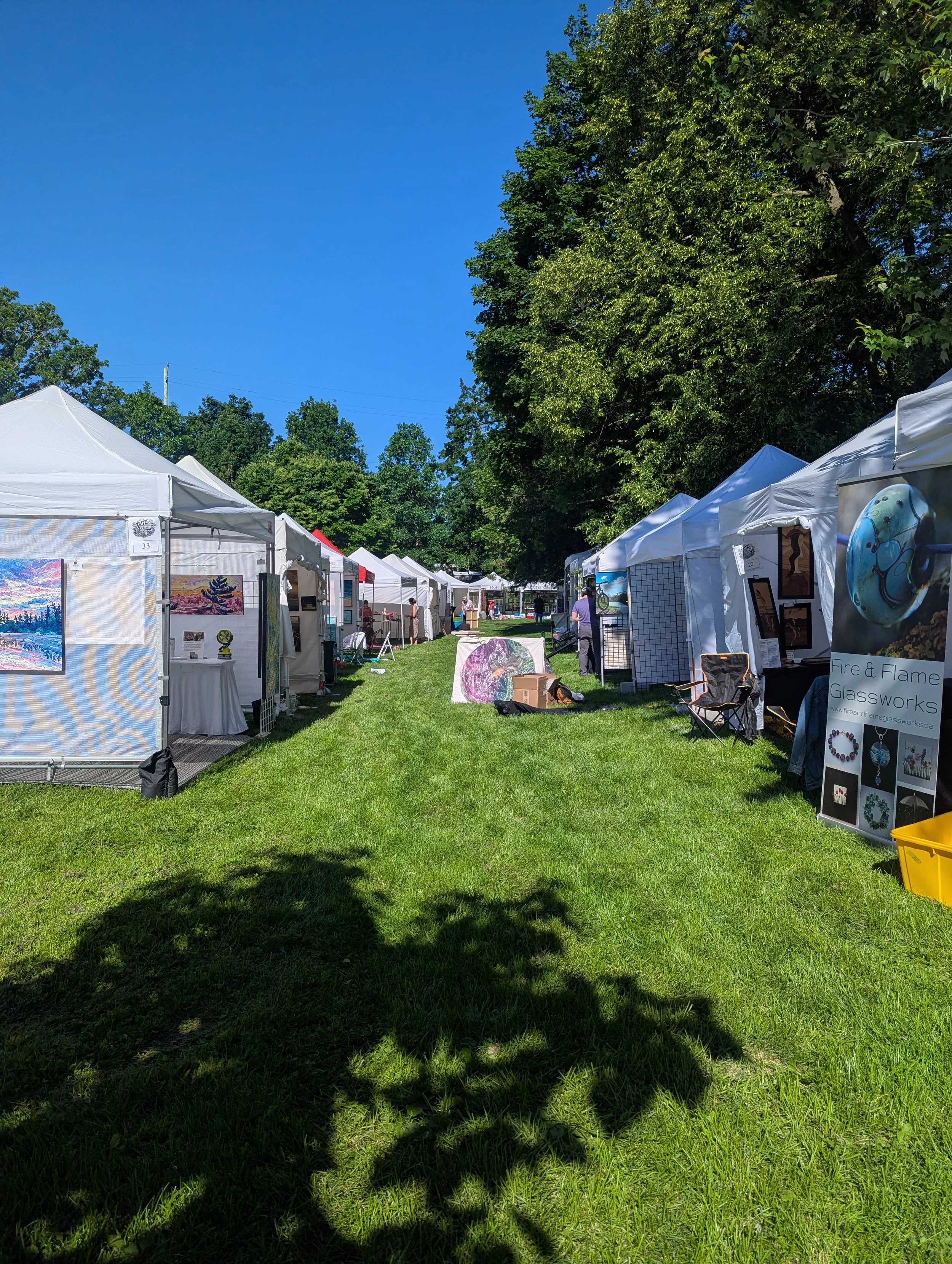 Des tentes d'artistes blanches installées dans un parc sous un ciel bleu.