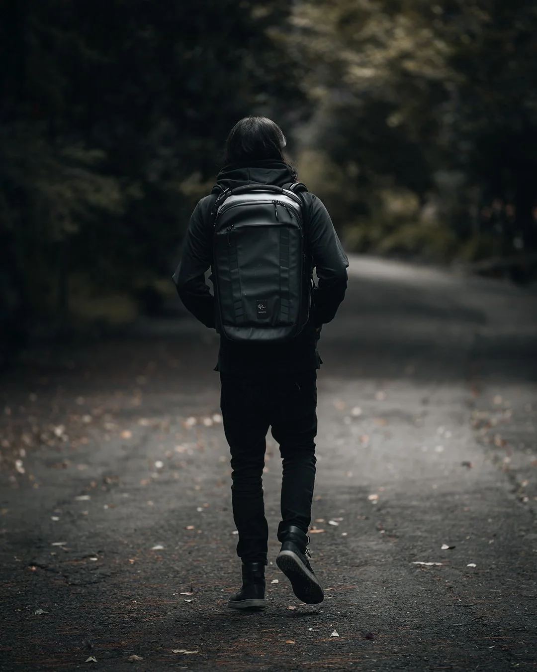 Fotografía lifestyle de marca, persona con mochila en sendero de bosque oscuro