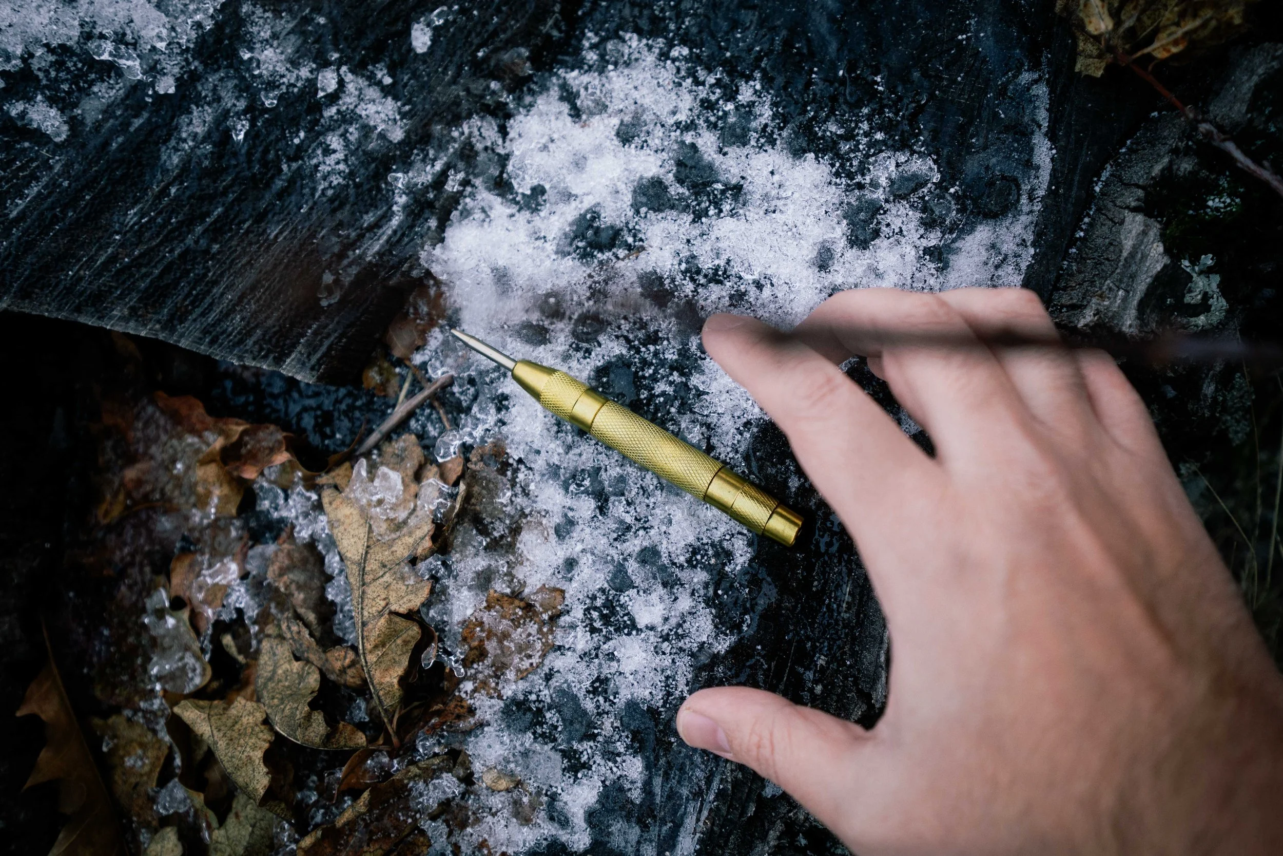 Fotografía de producto, bolígrafo táctico dorado sobre superficie helada con hojas de otoño