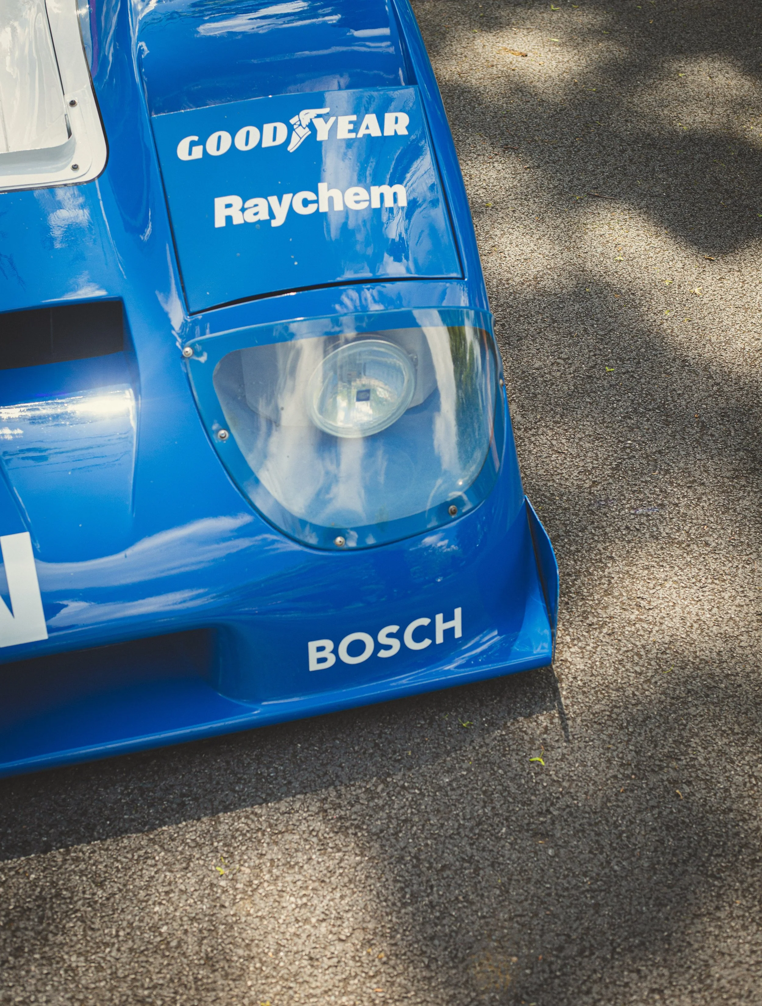 Close-up of a blue Nissan race car with 'Goodyear,' 'Raychem,' and 'Bosch' logos, showing the front nose and one headlight.