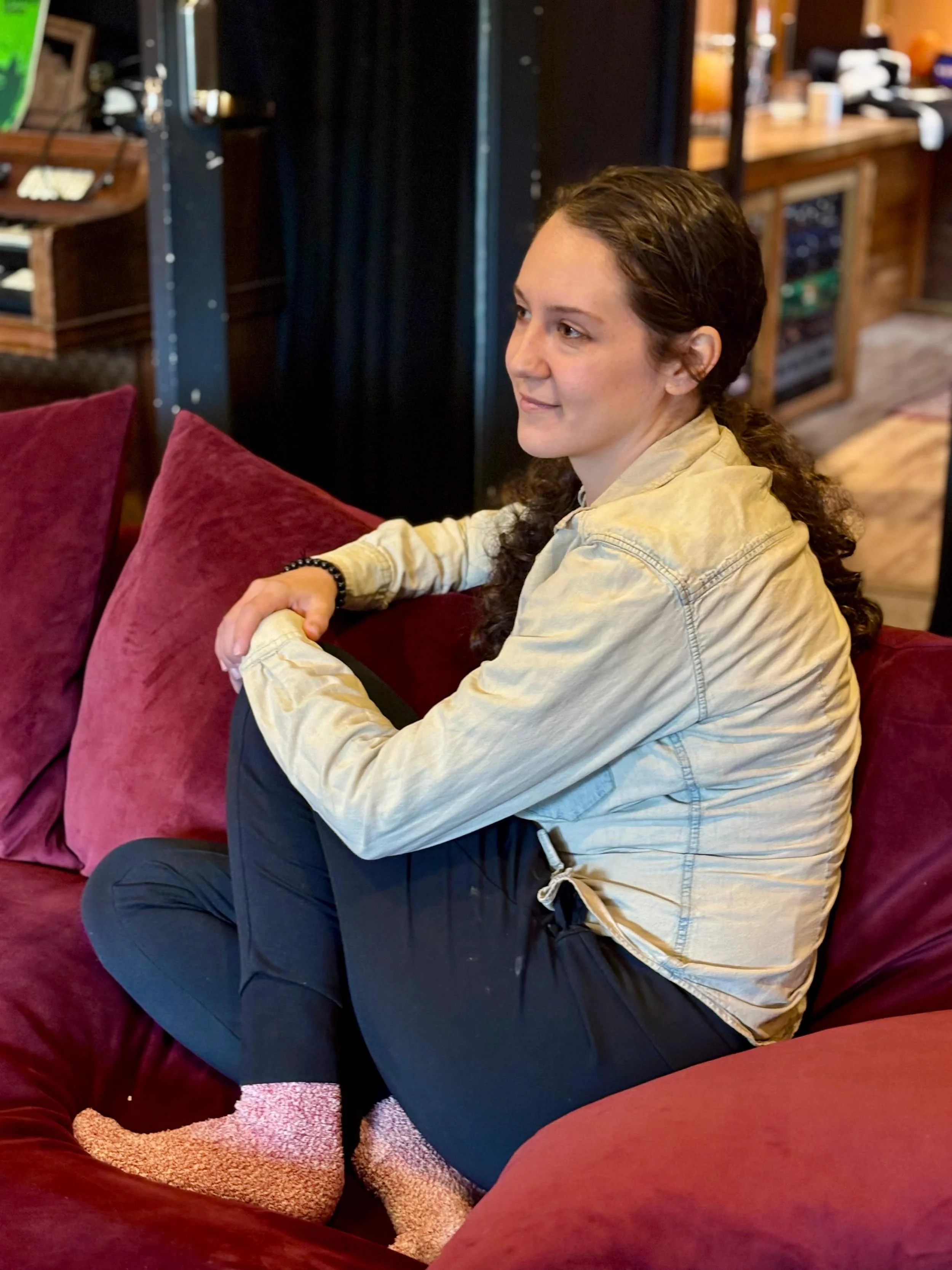 A smiling young lady  in front of audio recording and mixing equipment and speakers in a home studio.