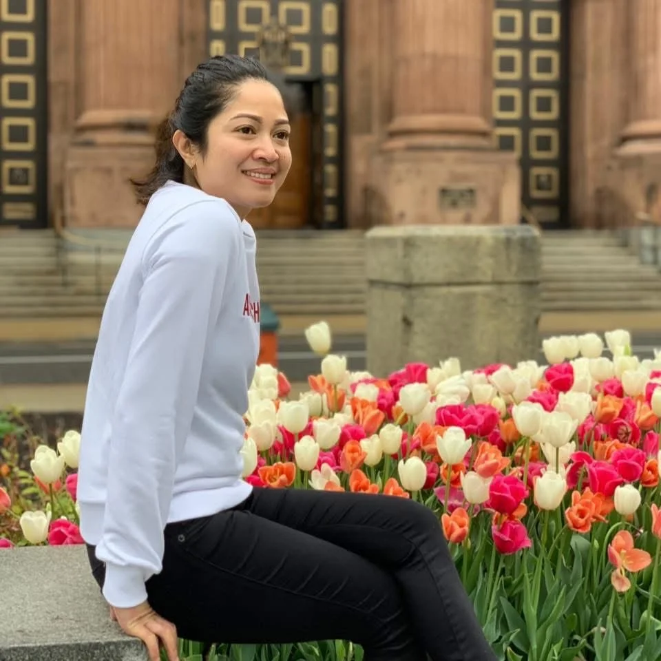 A woman sitting on a stone edge surrounded by colorful tulips in front of a historic building with ornate wooden doors and intricate patterns.