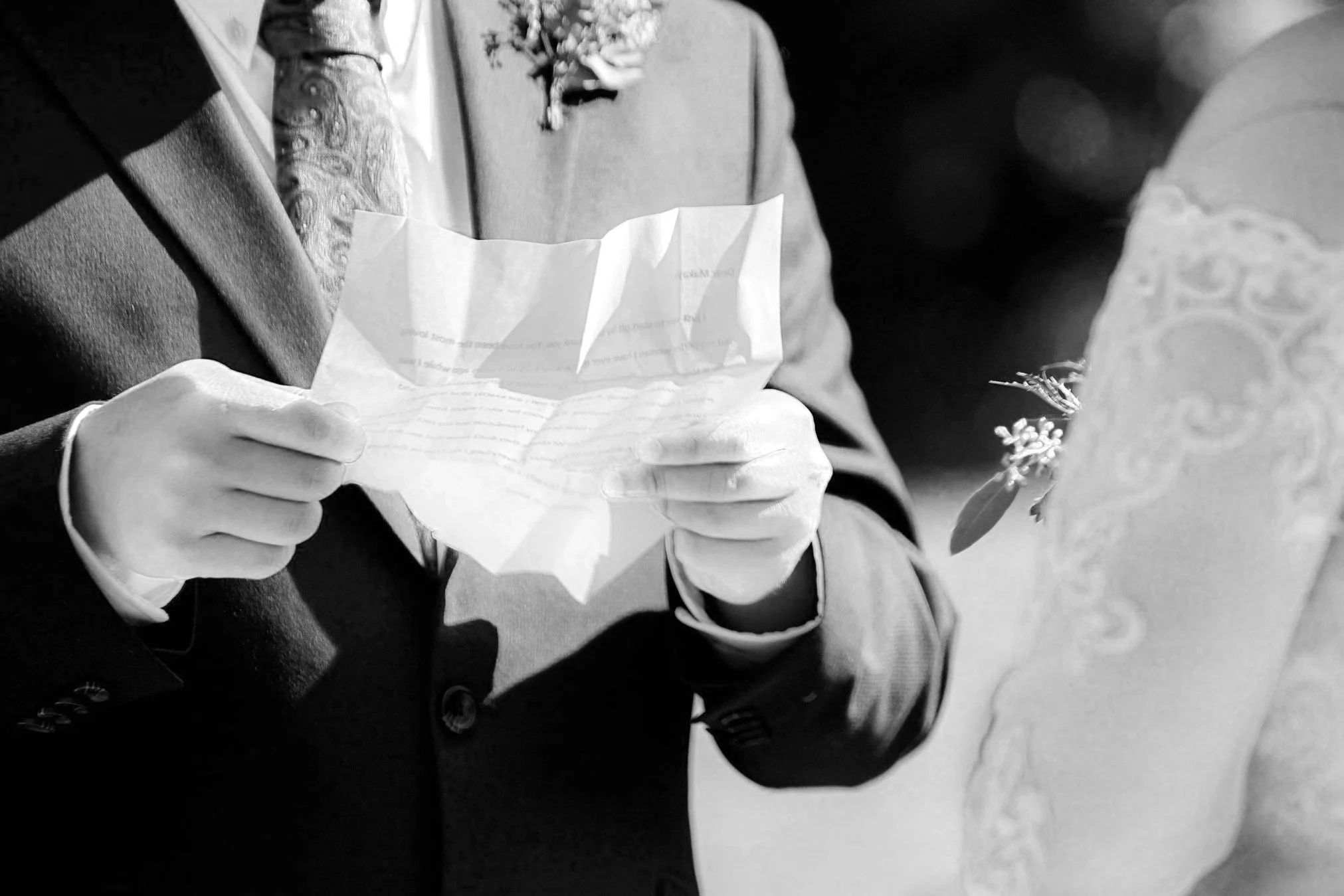 Bride and groom exchanging vows; groom holding a crumpled paper while standing with bride in lace dress.